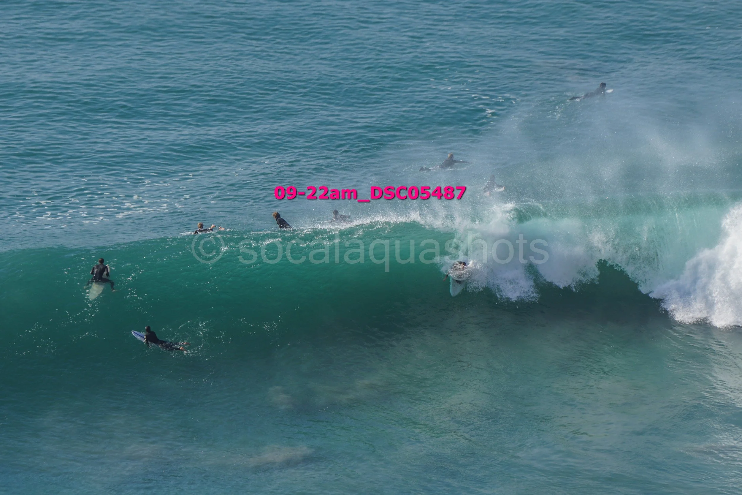 Surfers riding and paddling on large ocean waves in a clear blue sea.