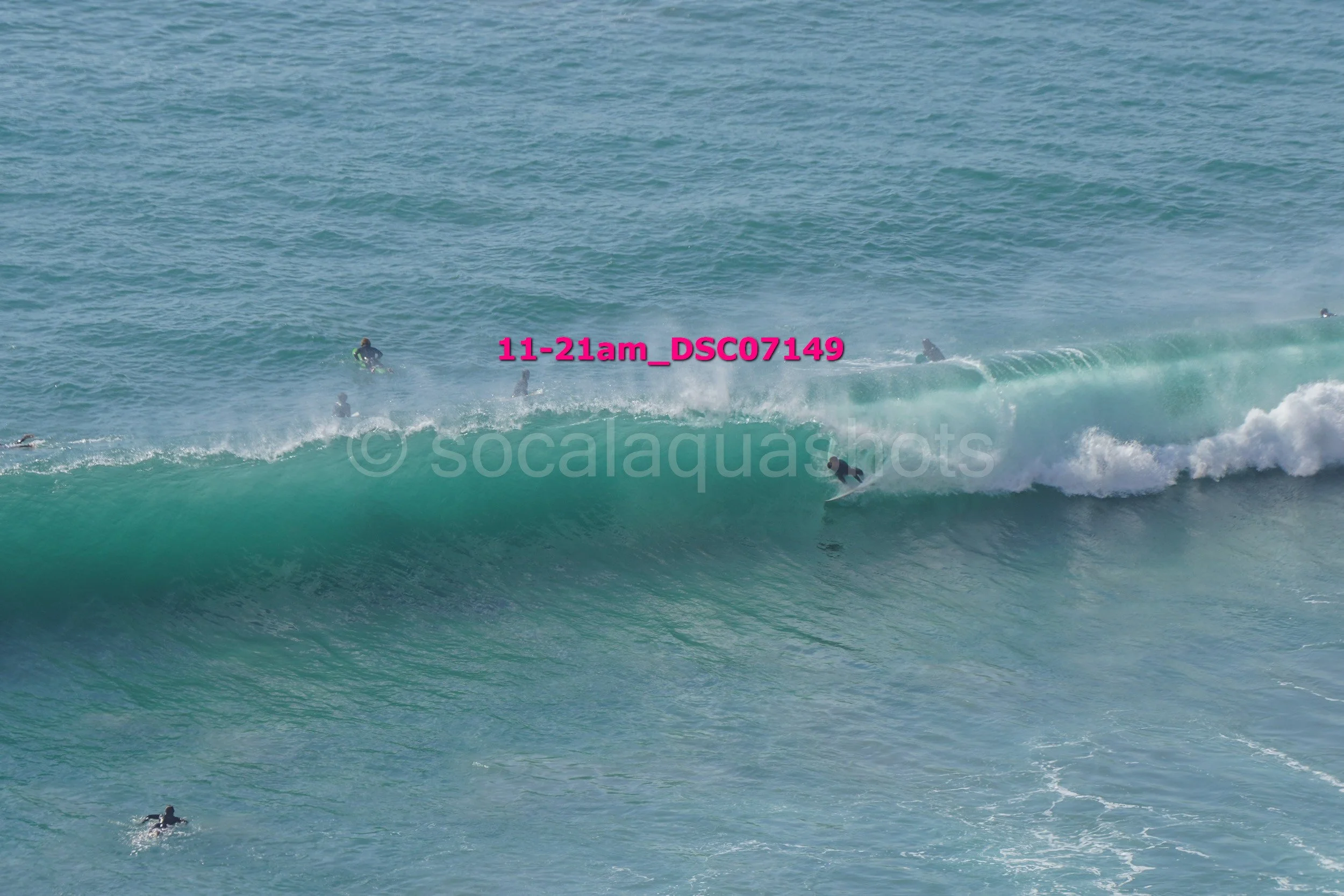 Surfers riding a large wave in the ocean with some surfers waiting in the water.