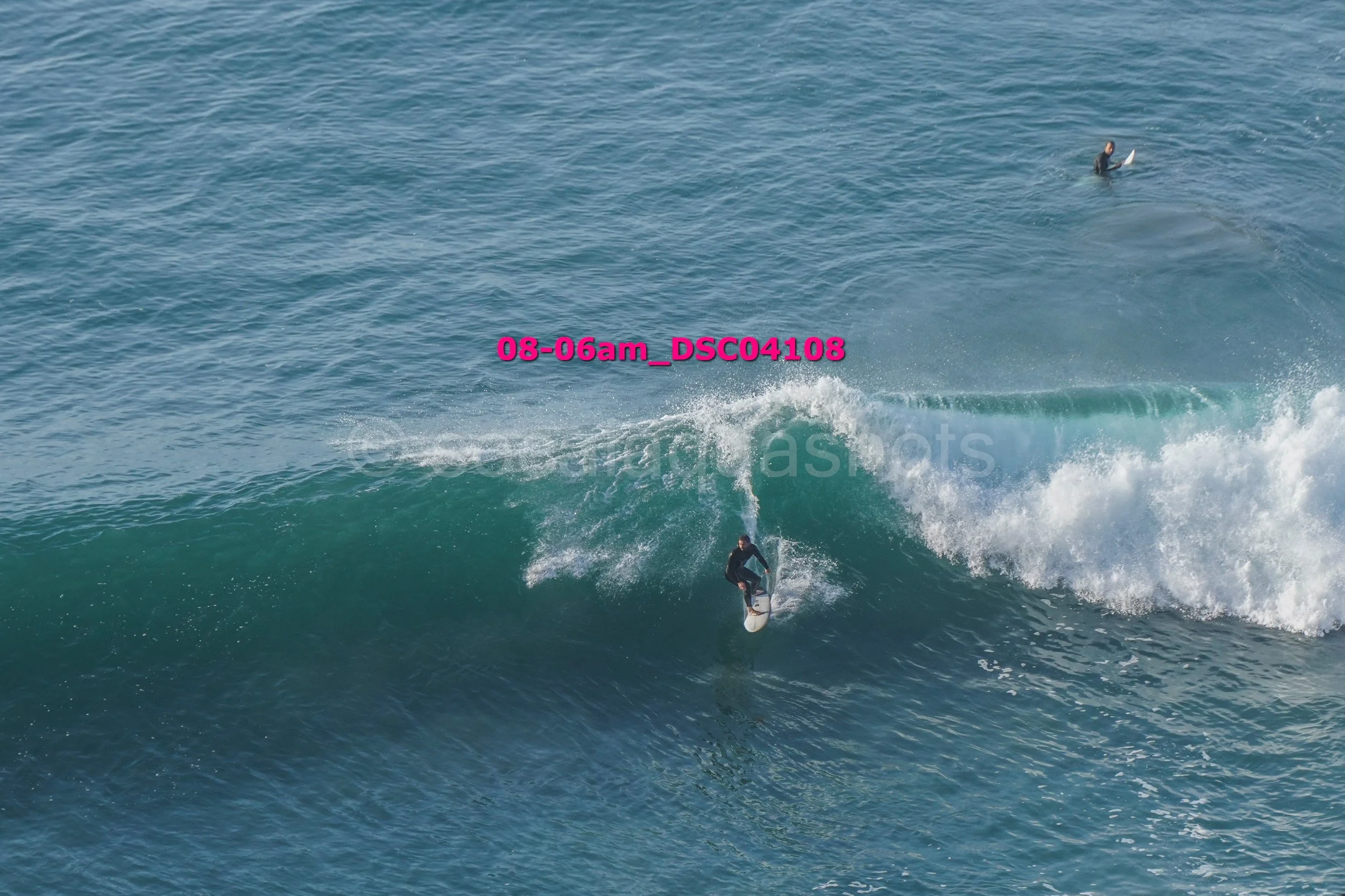 A surfer riding a wave in the ocean with another person surfing in the distance.
