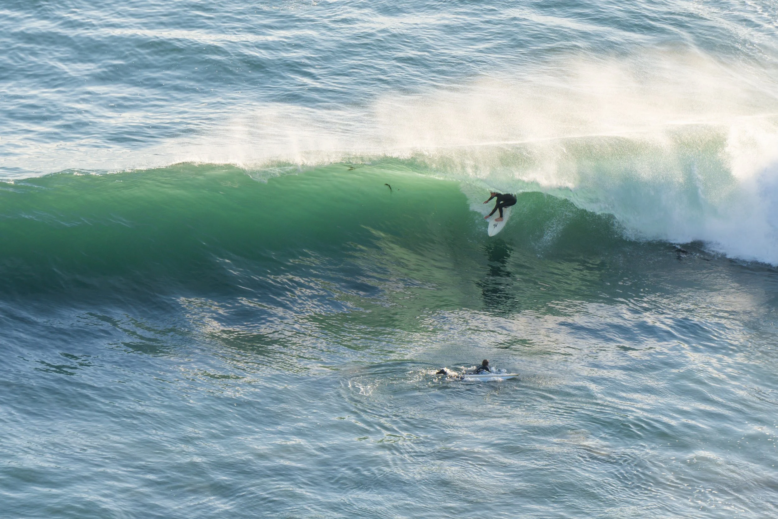 A surfer riding a large green wave while another surfer paddles in the water nearby.