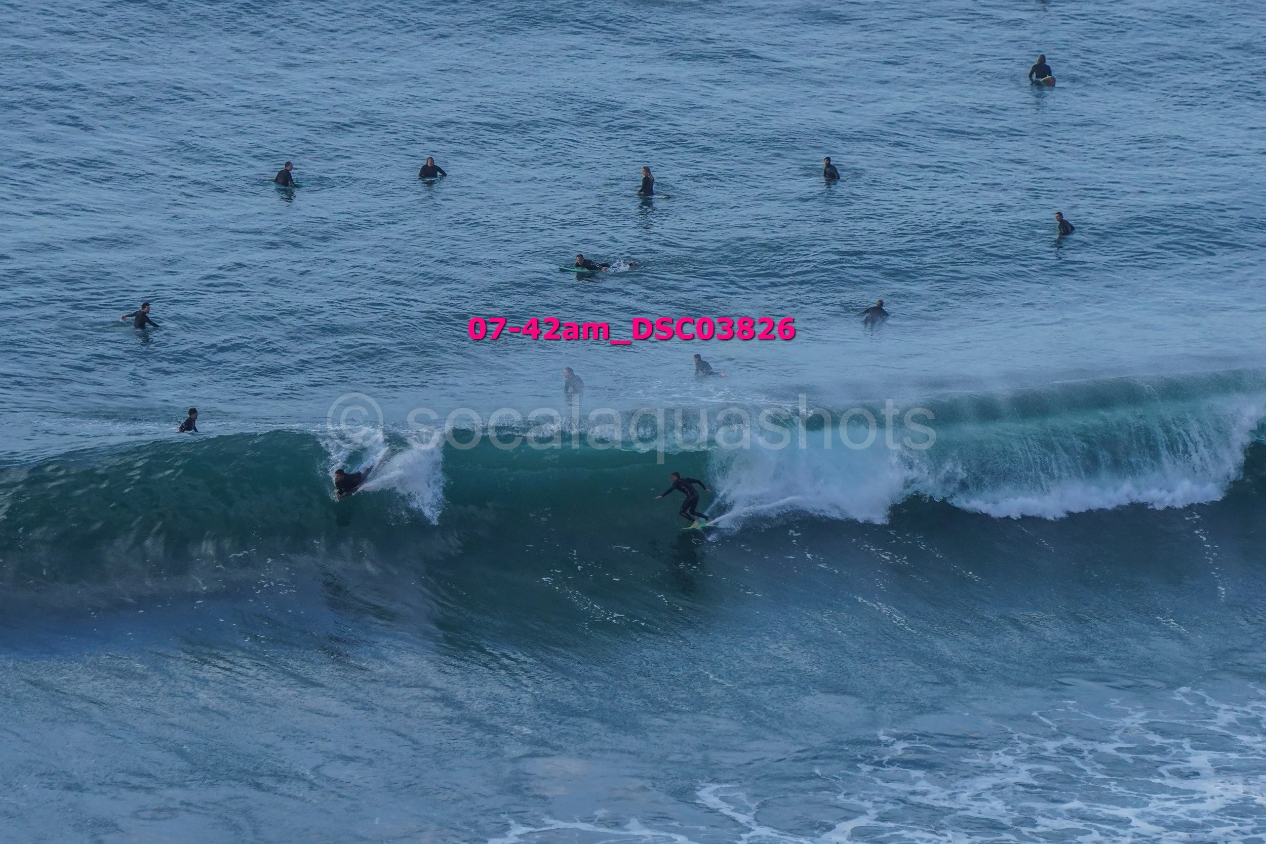 Surfer riding a large wave with multiple surfers in the water in the background near the coast.