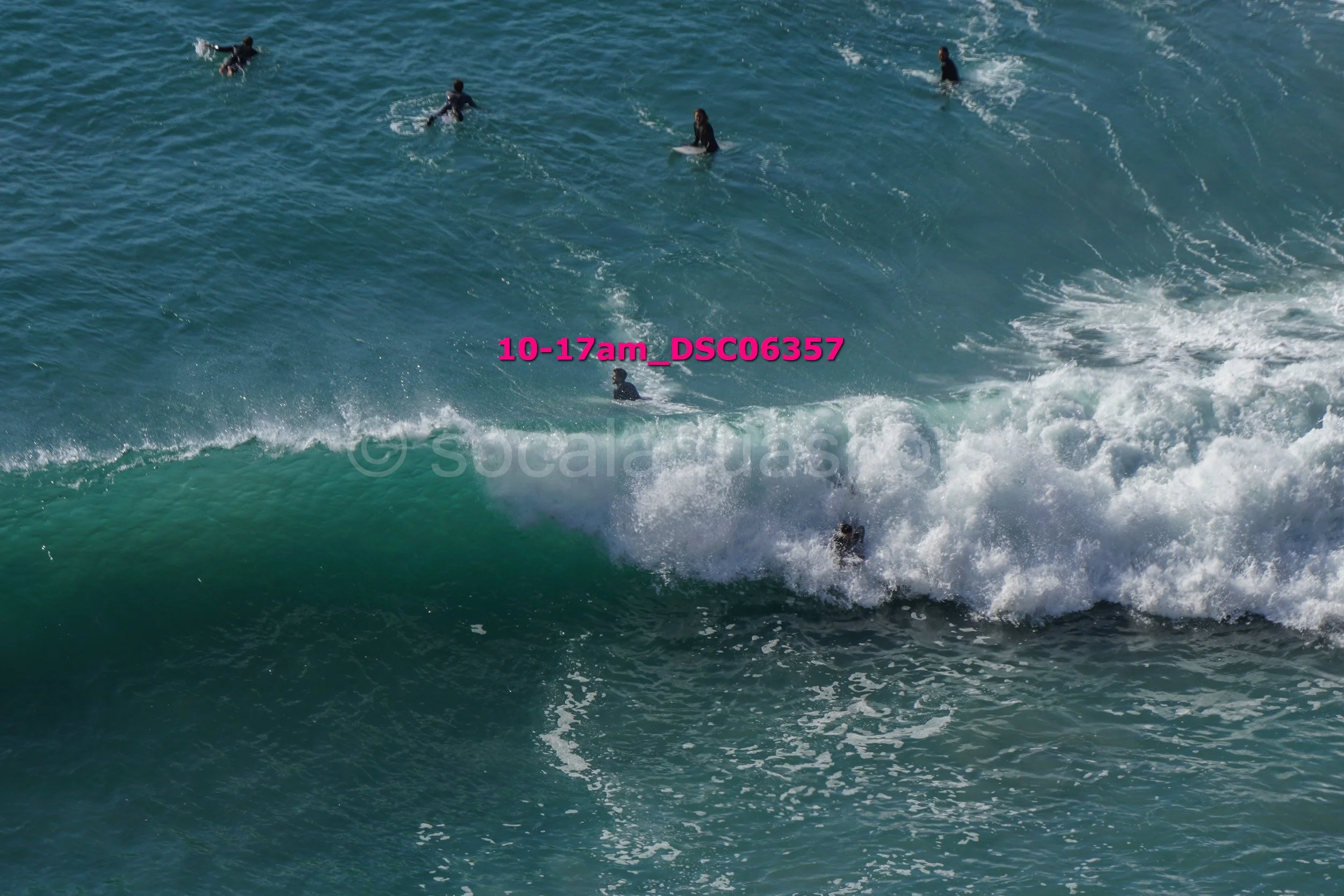 People surfing in the ocean near a breaking wave.