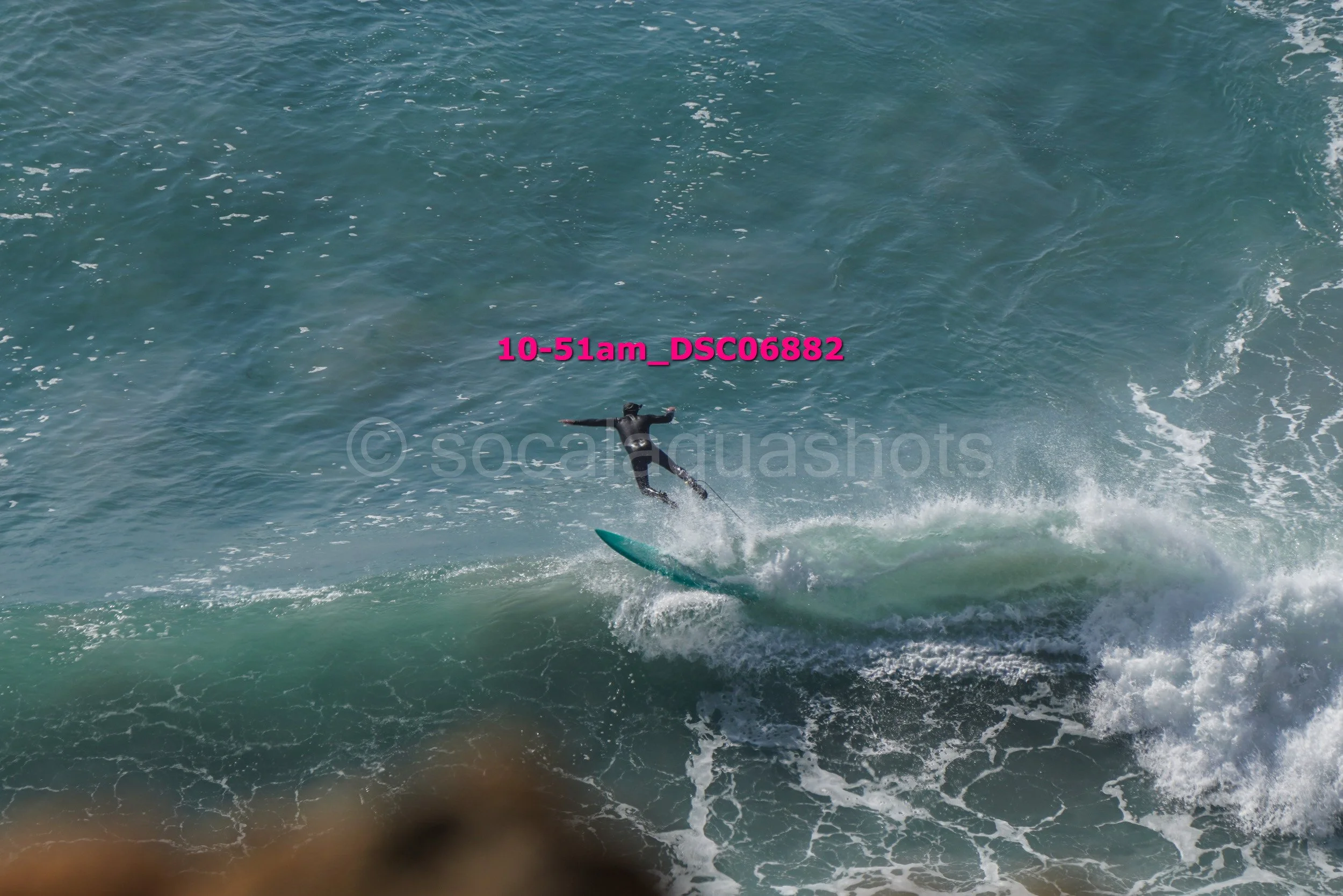A person surfing on a large ocean wave wearing a black wetsuit.