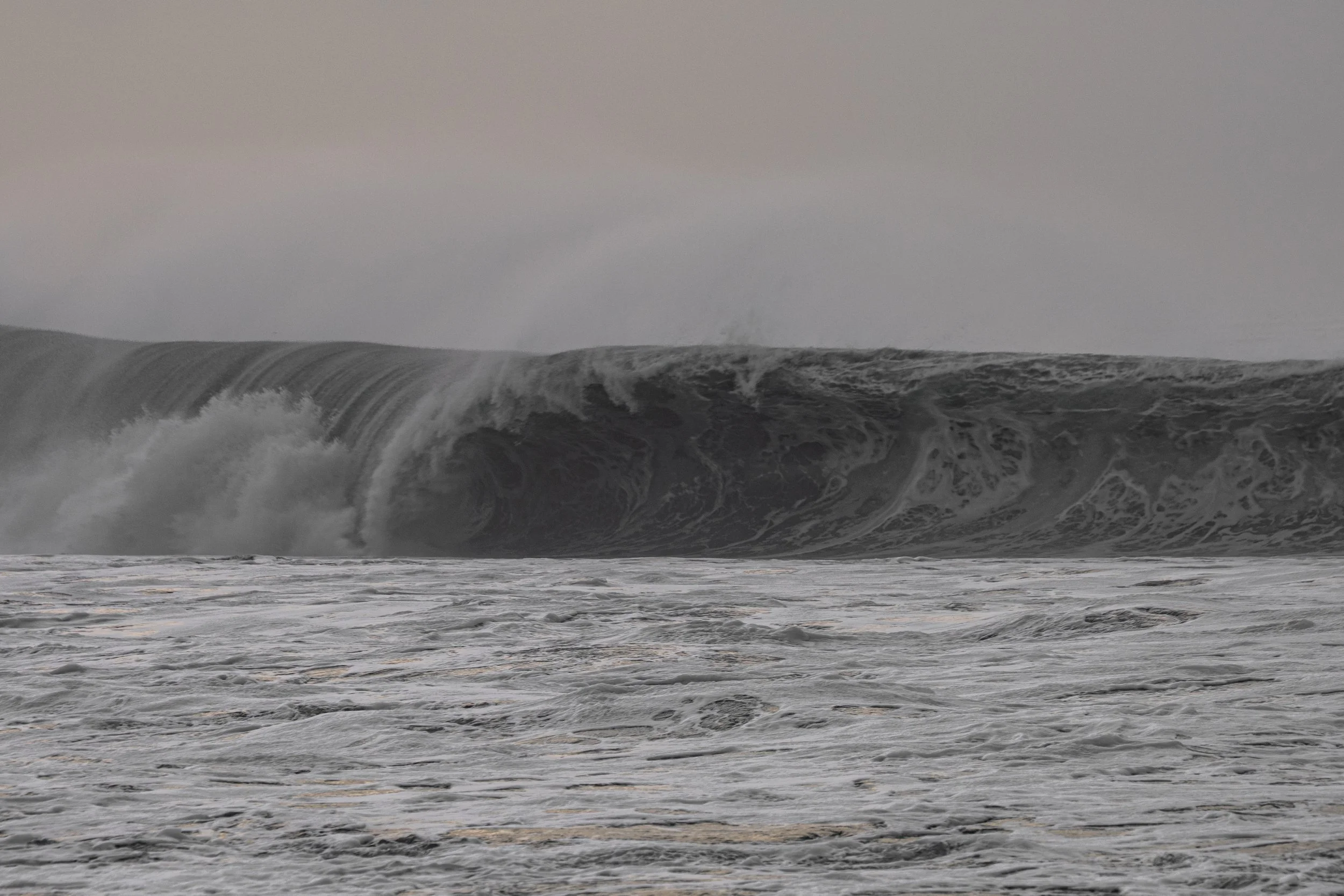 Dark gray ocean waves crashing under an overcast sky.