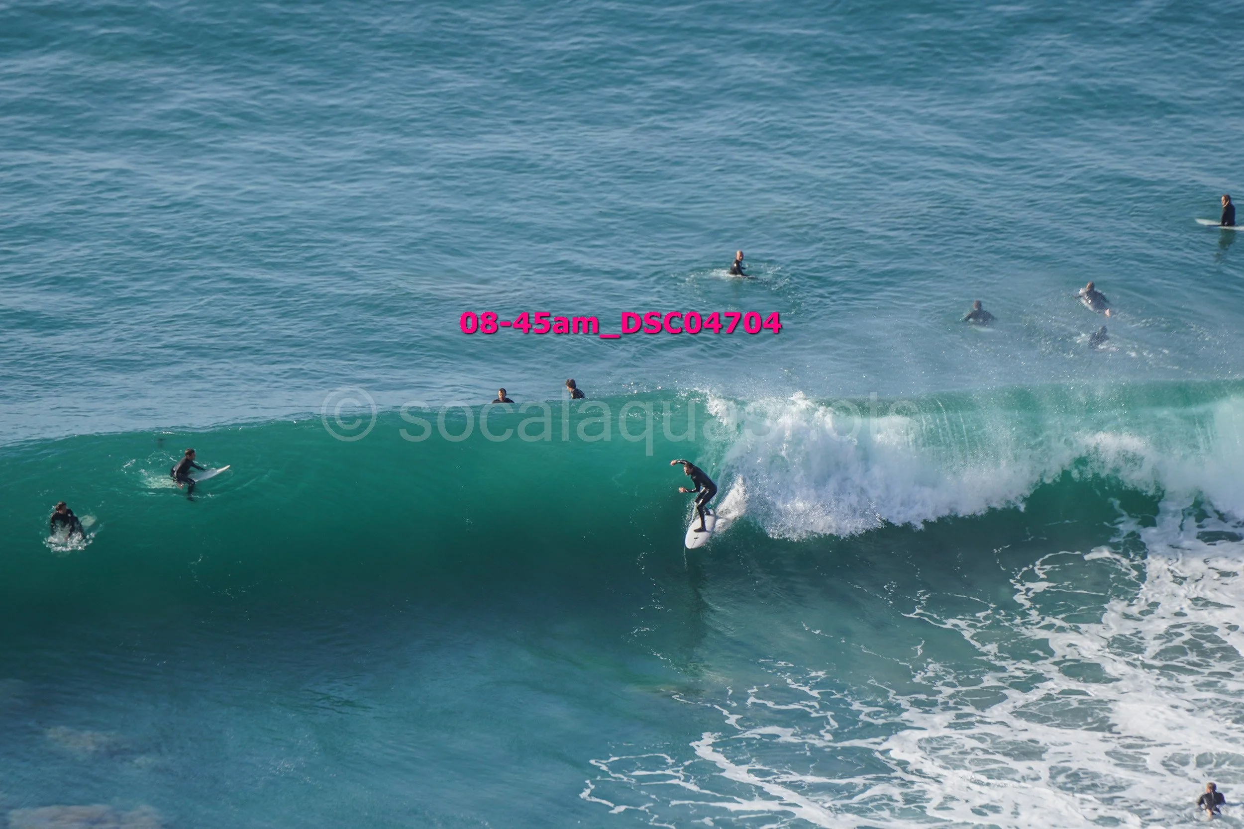 Surfer riding a wave with several people in wetsuits surfing and swimming in the background