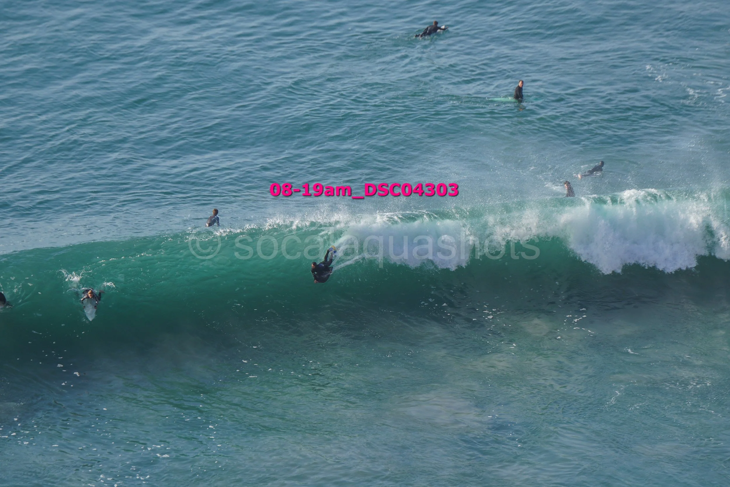 Surfers in wetsuits riding and paddling on ocean waves.