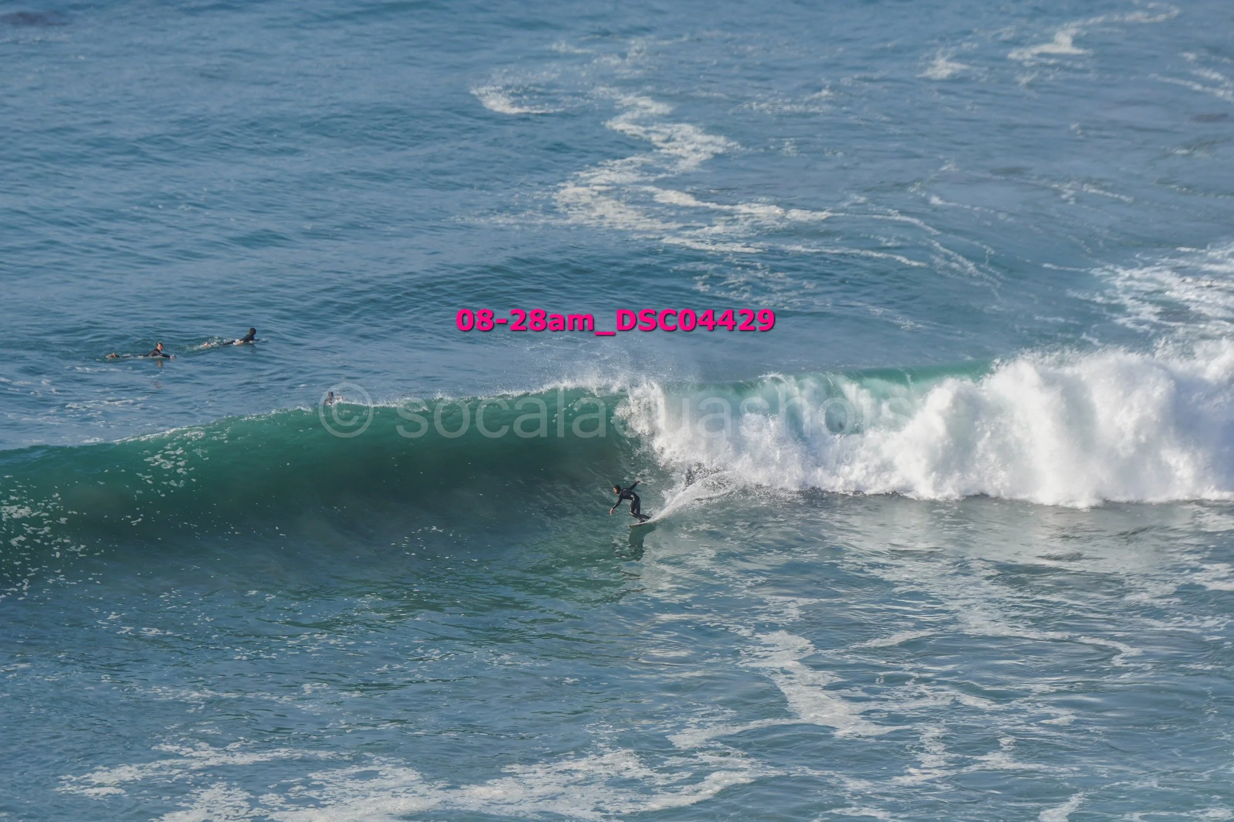 A person surfing on a wave in the ocean, with two other surfers floating in the water nearby.