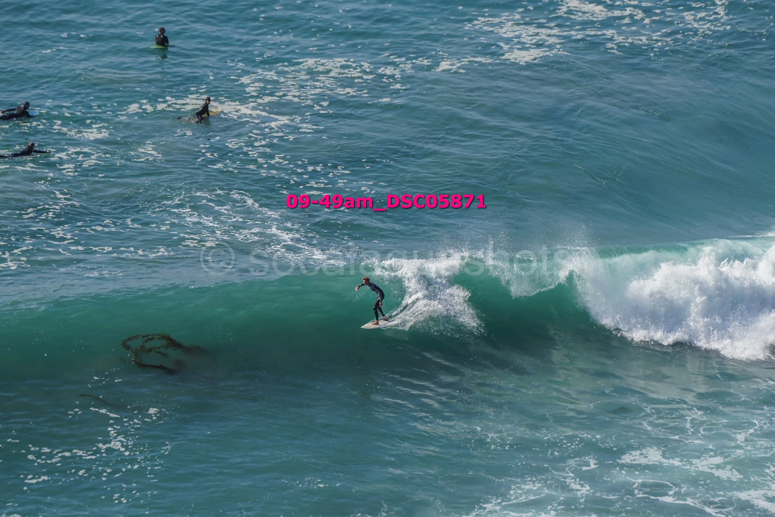 Surfer riding a wave with several surfers in the water watching.