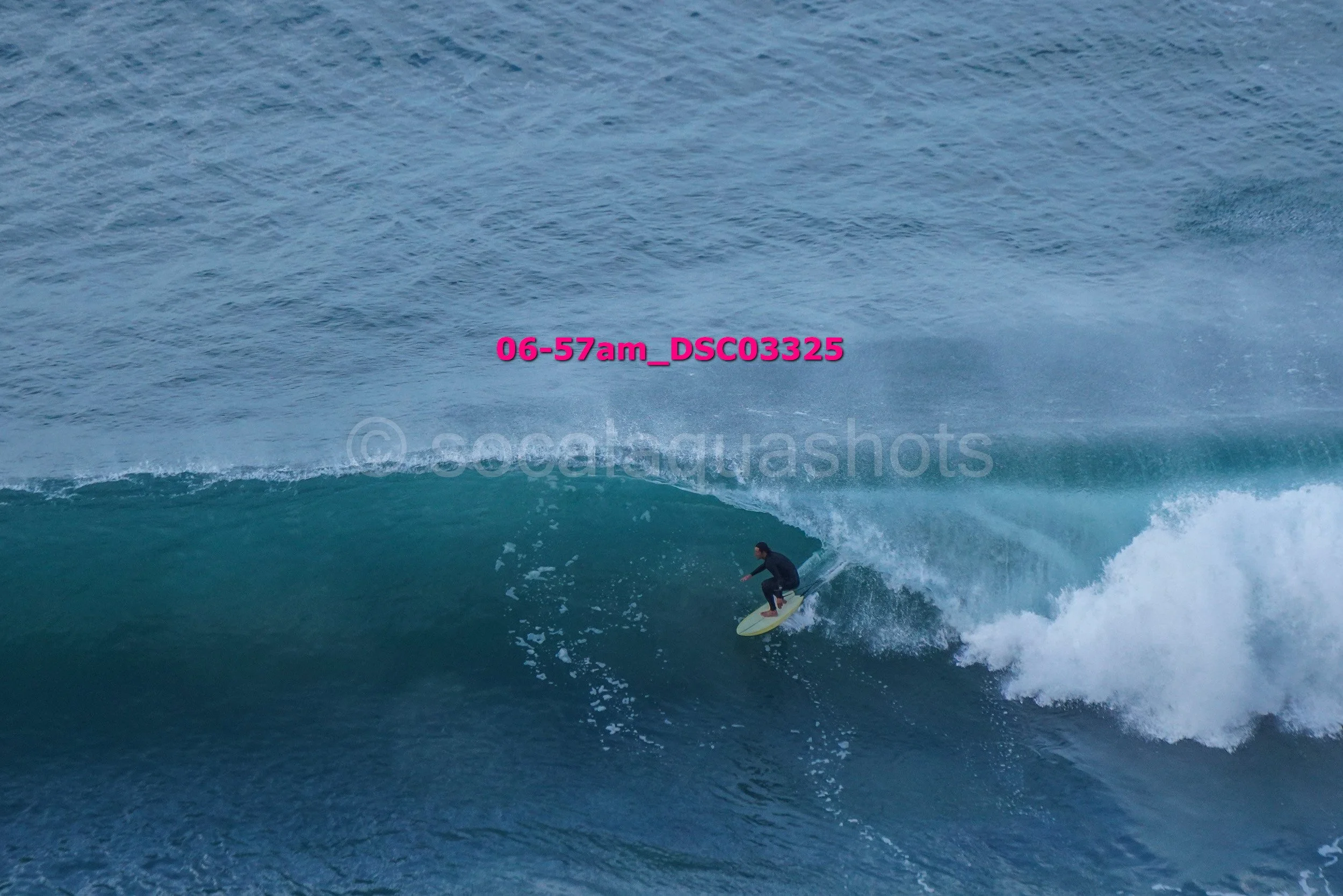 A person surfing on a large ocean wave during daylight with a mist of water in the background.