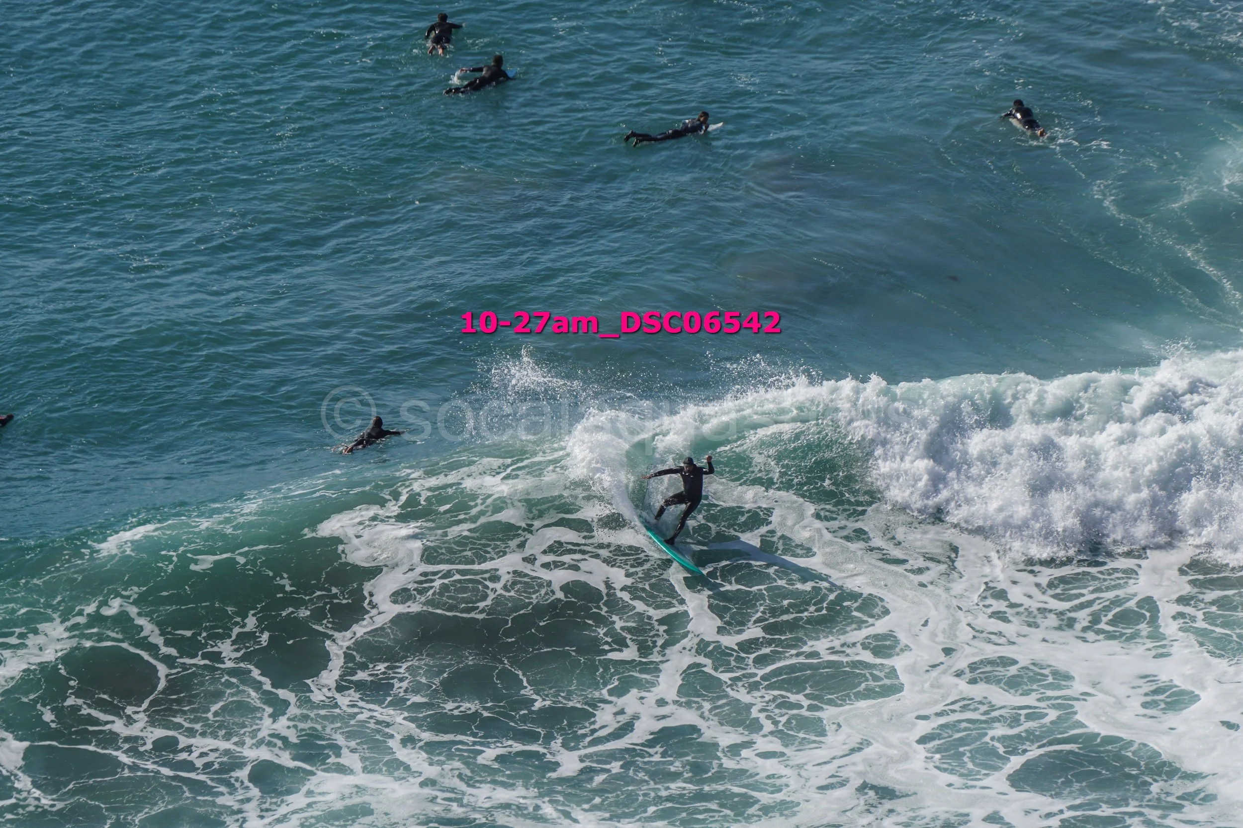 Surfer riding a wave with multiple surfers swimming in the ocean nearby.