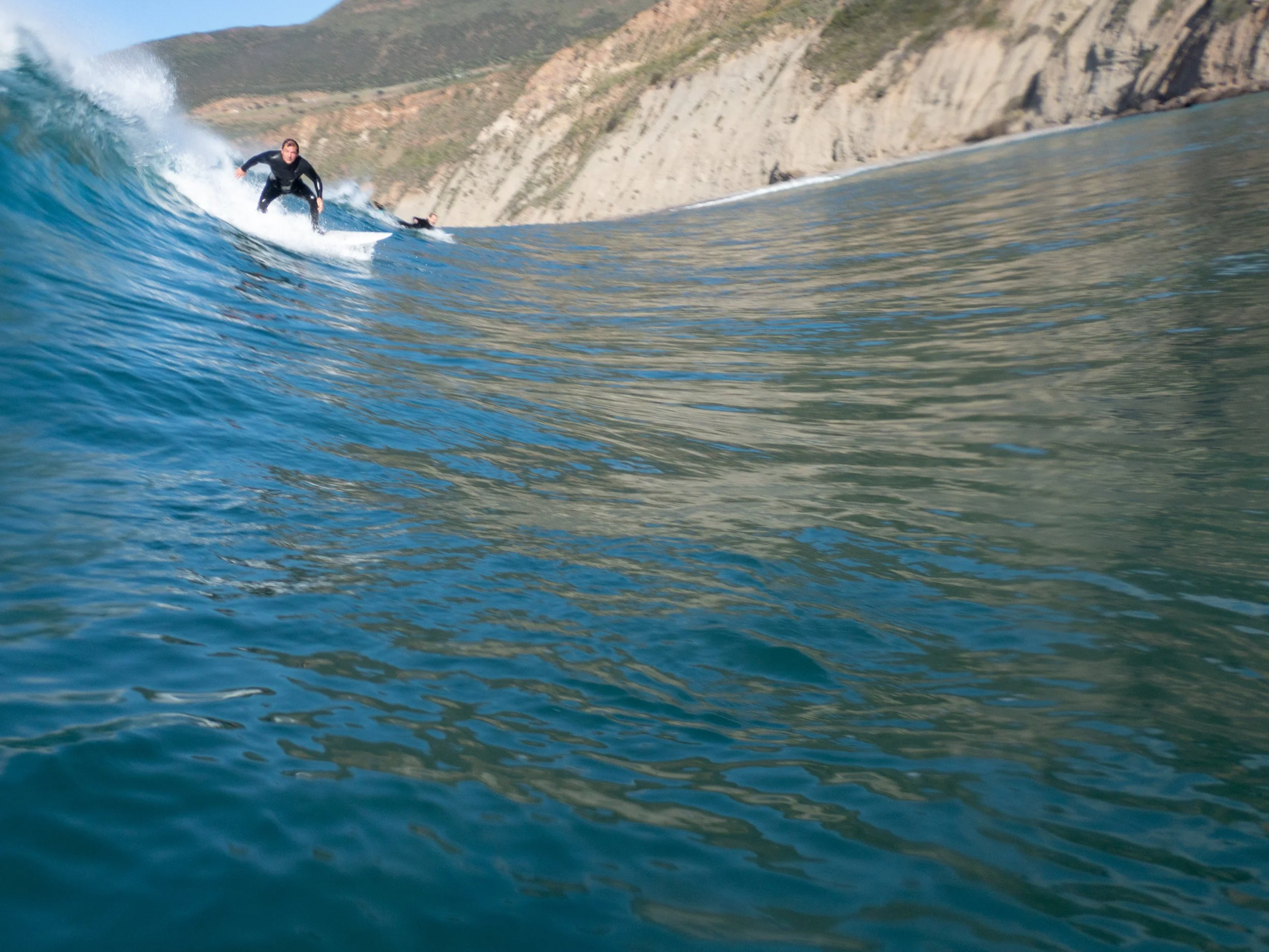 Surfer riding a large wave near rocky cliffs.