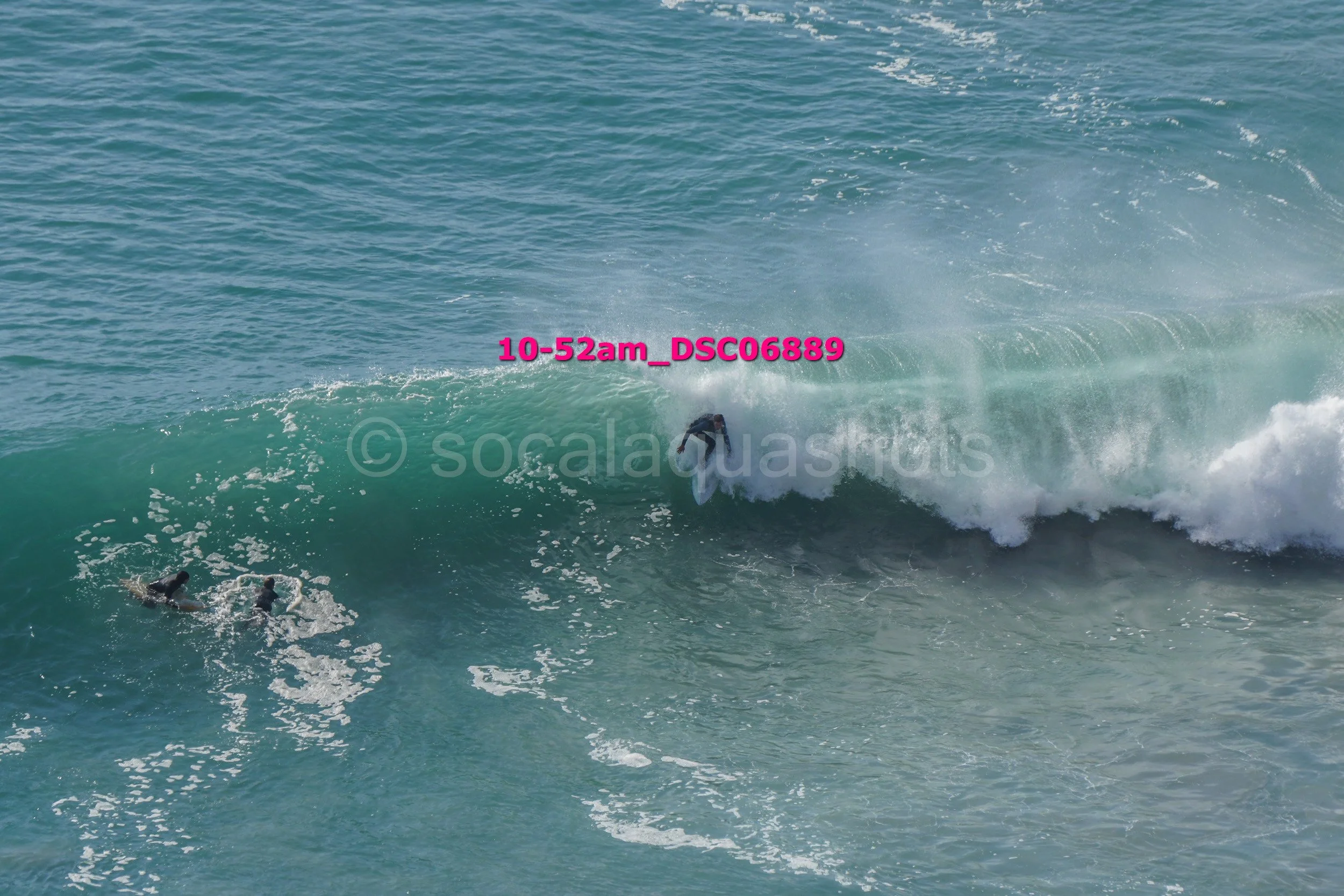 A person surfing on a wave with two additional surfers in the water nearby.