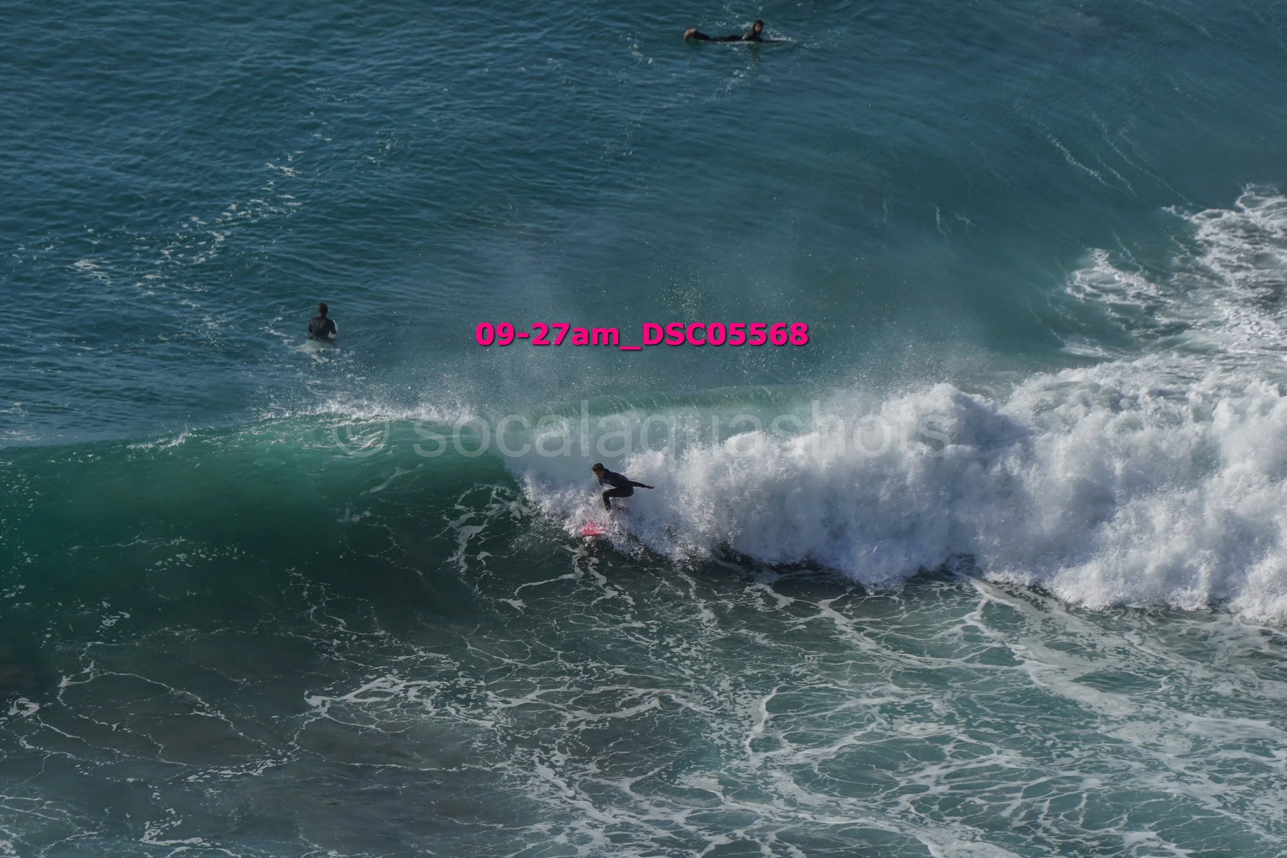 Surfer riding a wave in the ocean with two other surfers in the water nearby.