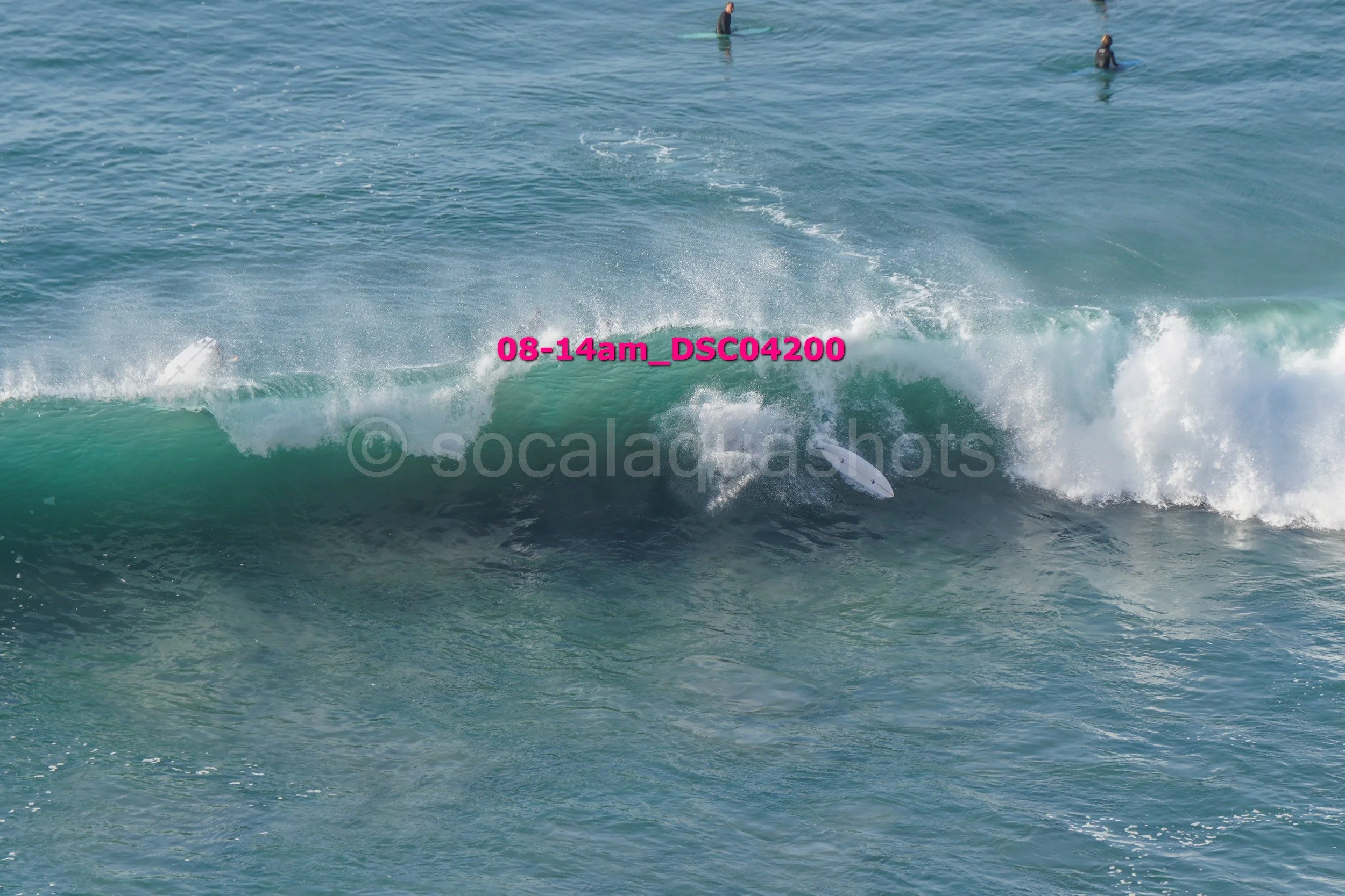 Surfboards falling off a breaking wave in the ocean with two people swimming in the background.
