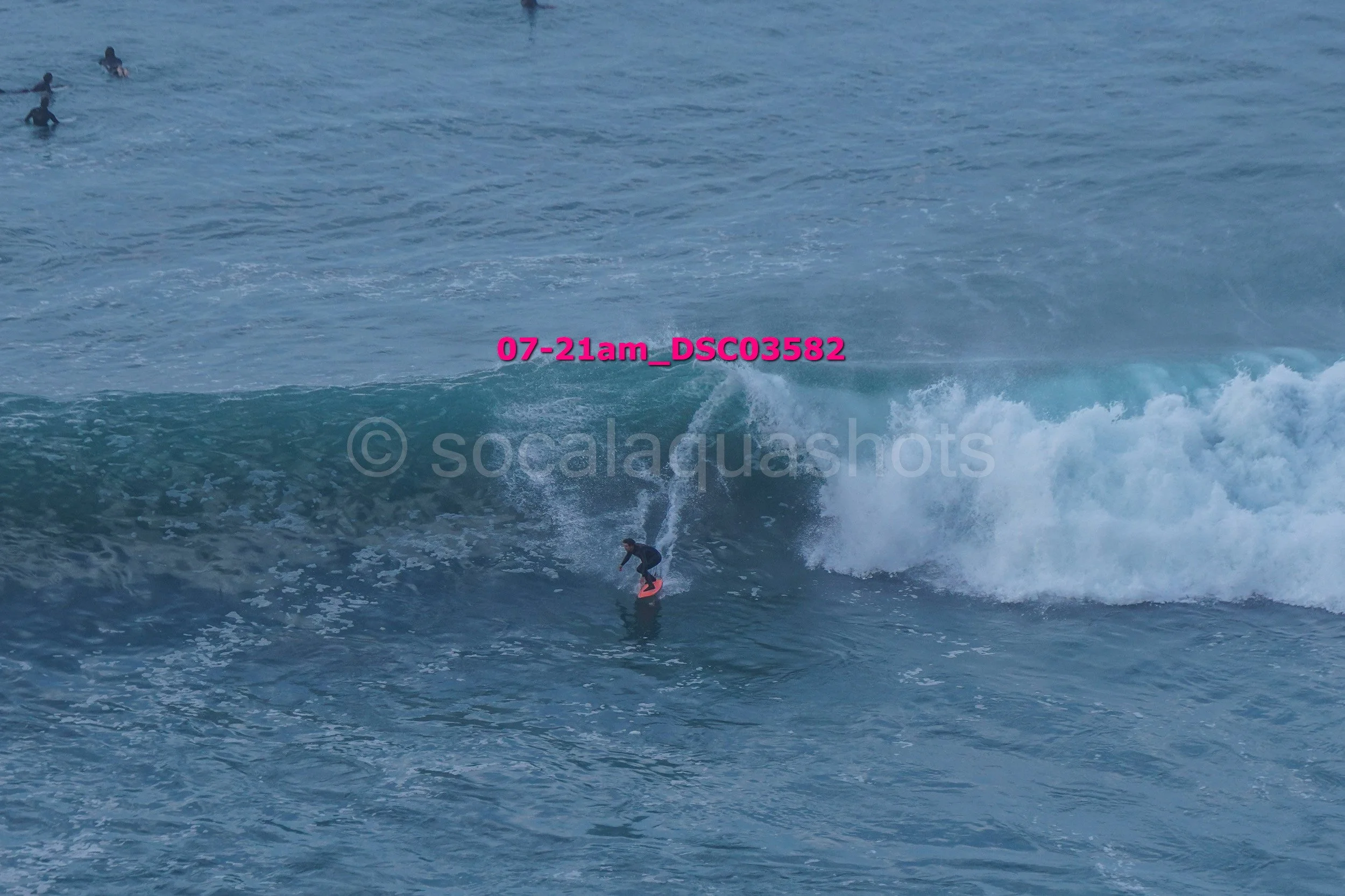 A person surfing on a wave in the ocean, with a few other surfers in the background.