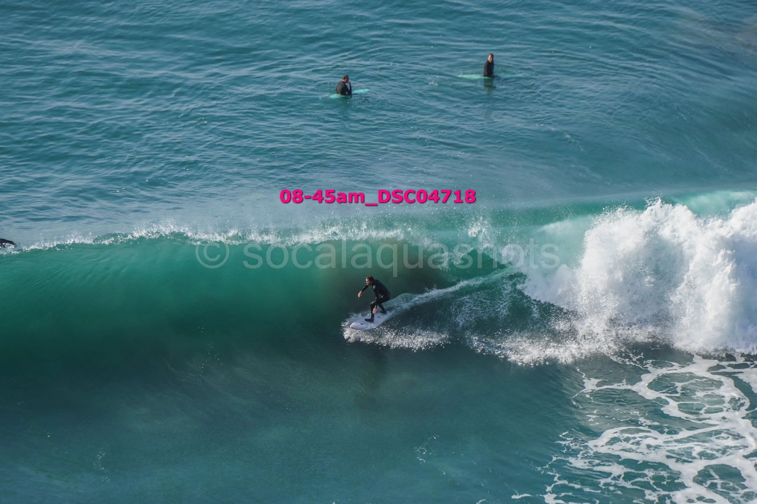 A person surfing on a wave in the ocean with two other surfers visible in the water in the background.