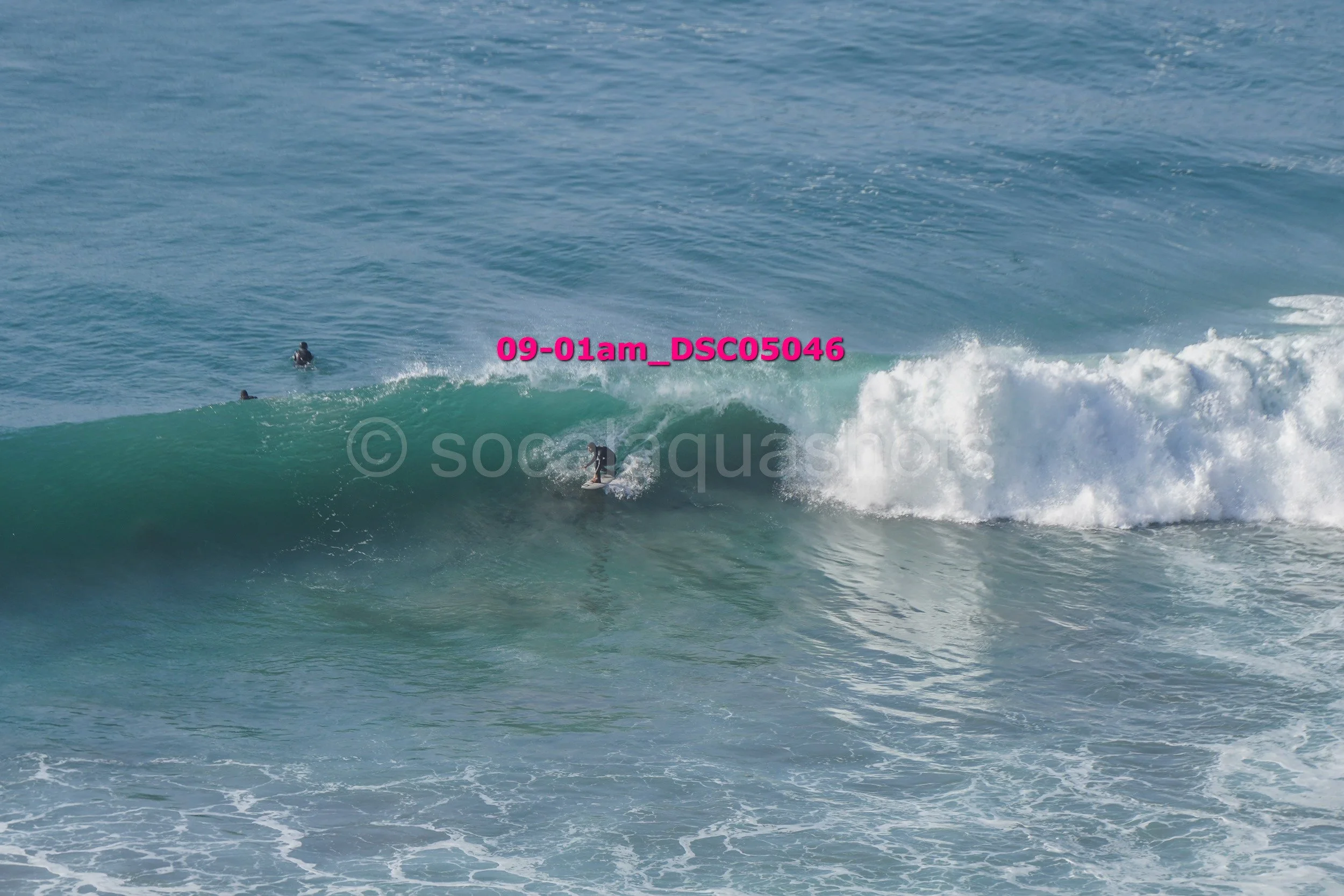 Surfer riding a wave in the ocean with three other surfers watching from behind.