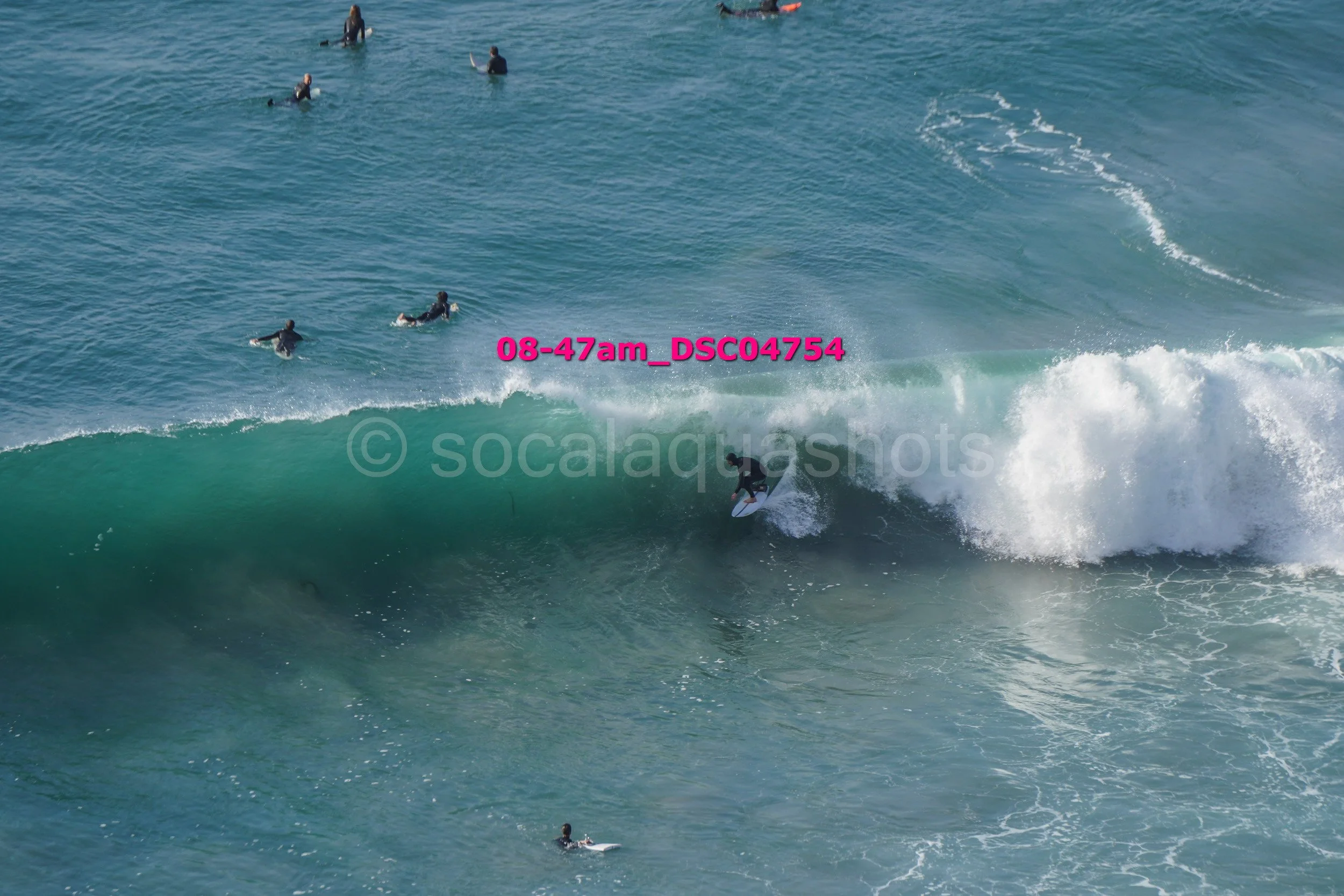 Surfer riding a large wave with several surfers in the water watching.