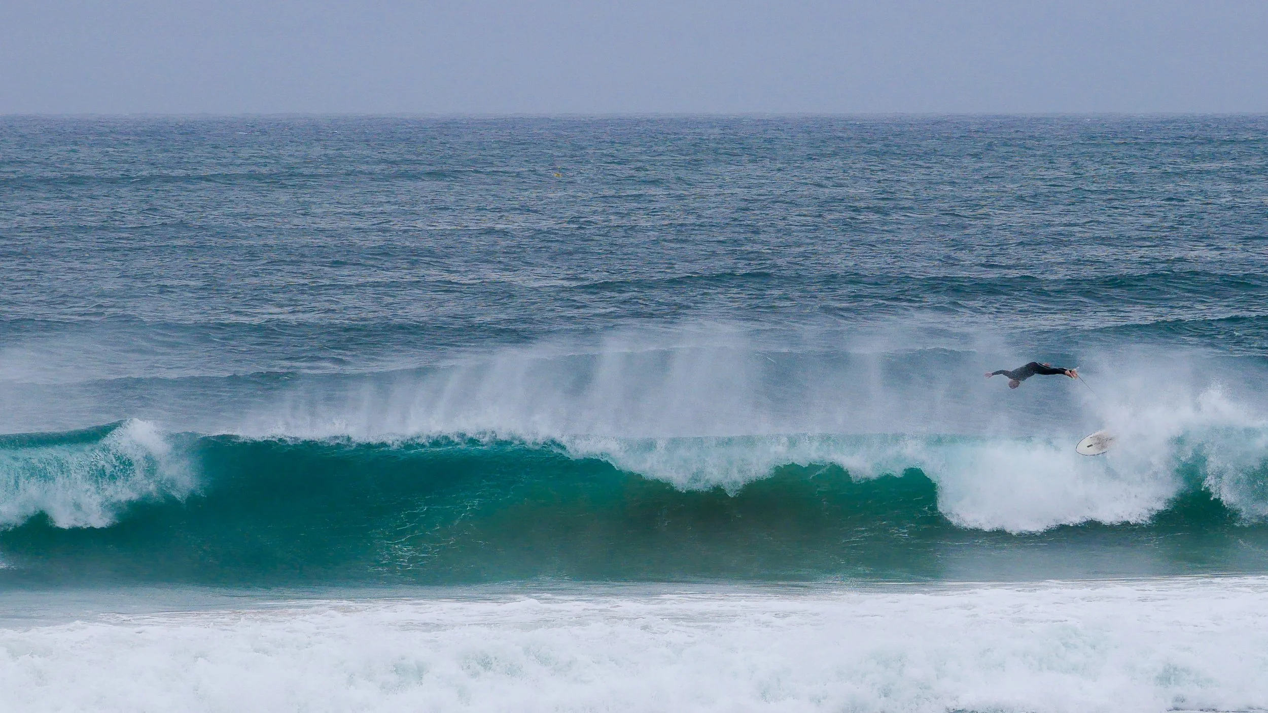 Surfer falling off surfboard amid large ocean wave