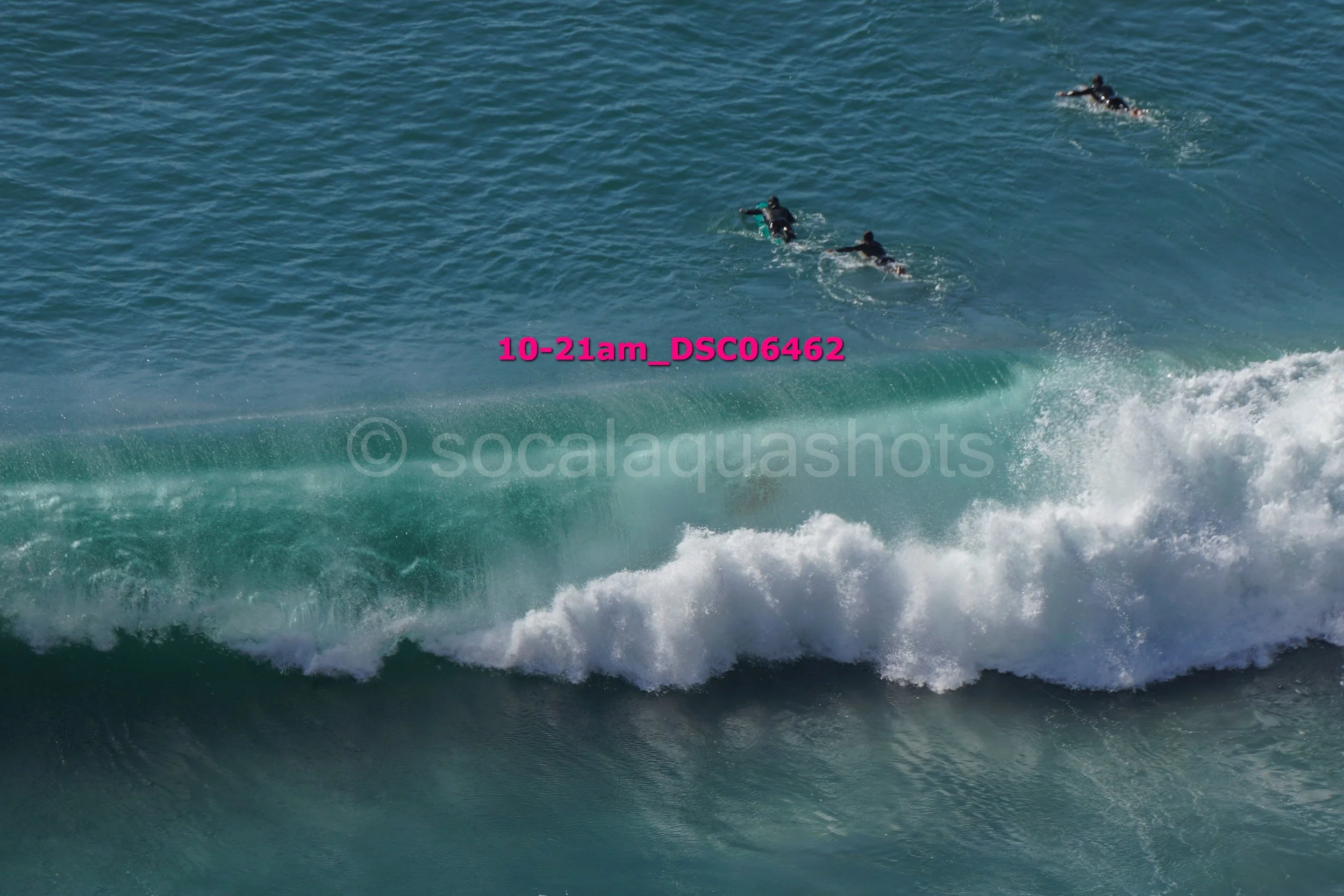 Three surfers in wetsuits riding a large ocean wave with white foam at the front.