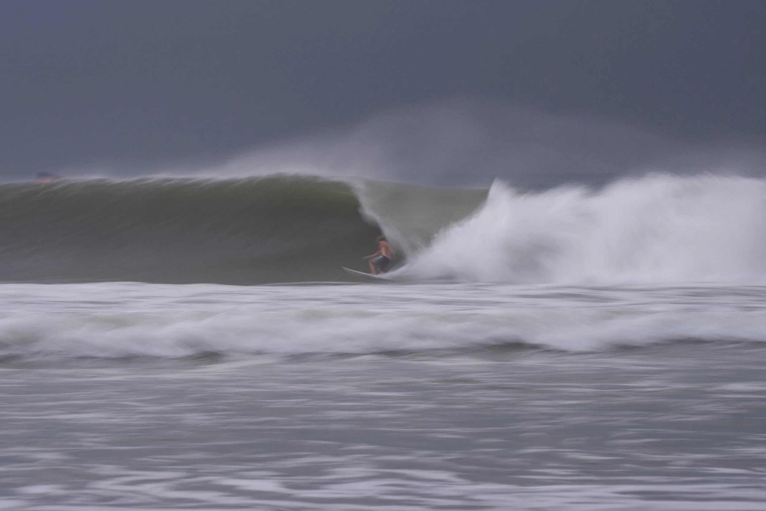 A person surfing on a large wave in the ocean during a stormy day with dark clouds overhead.