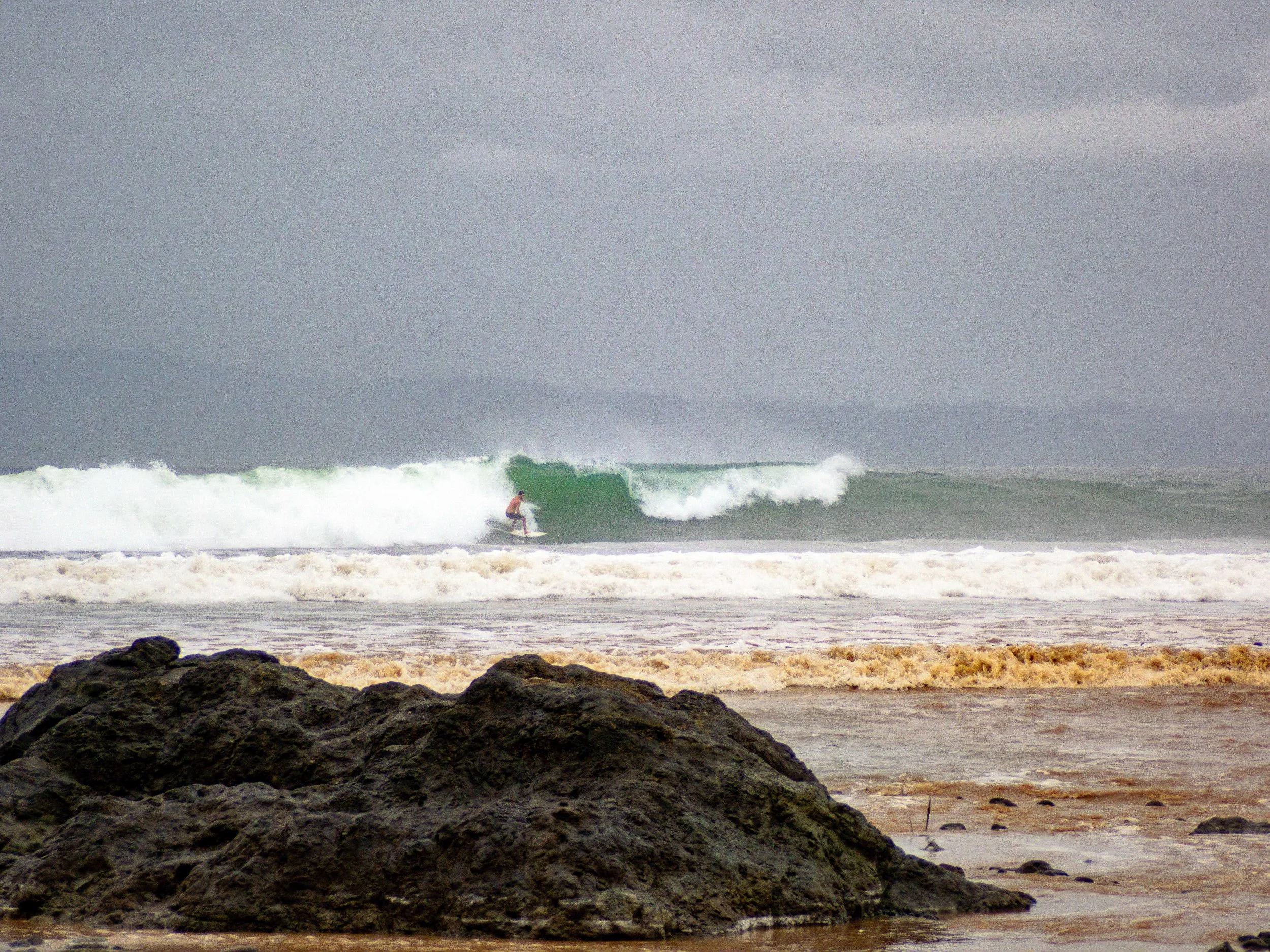 Surfer riding a wave near rocky shore on a cloudy day