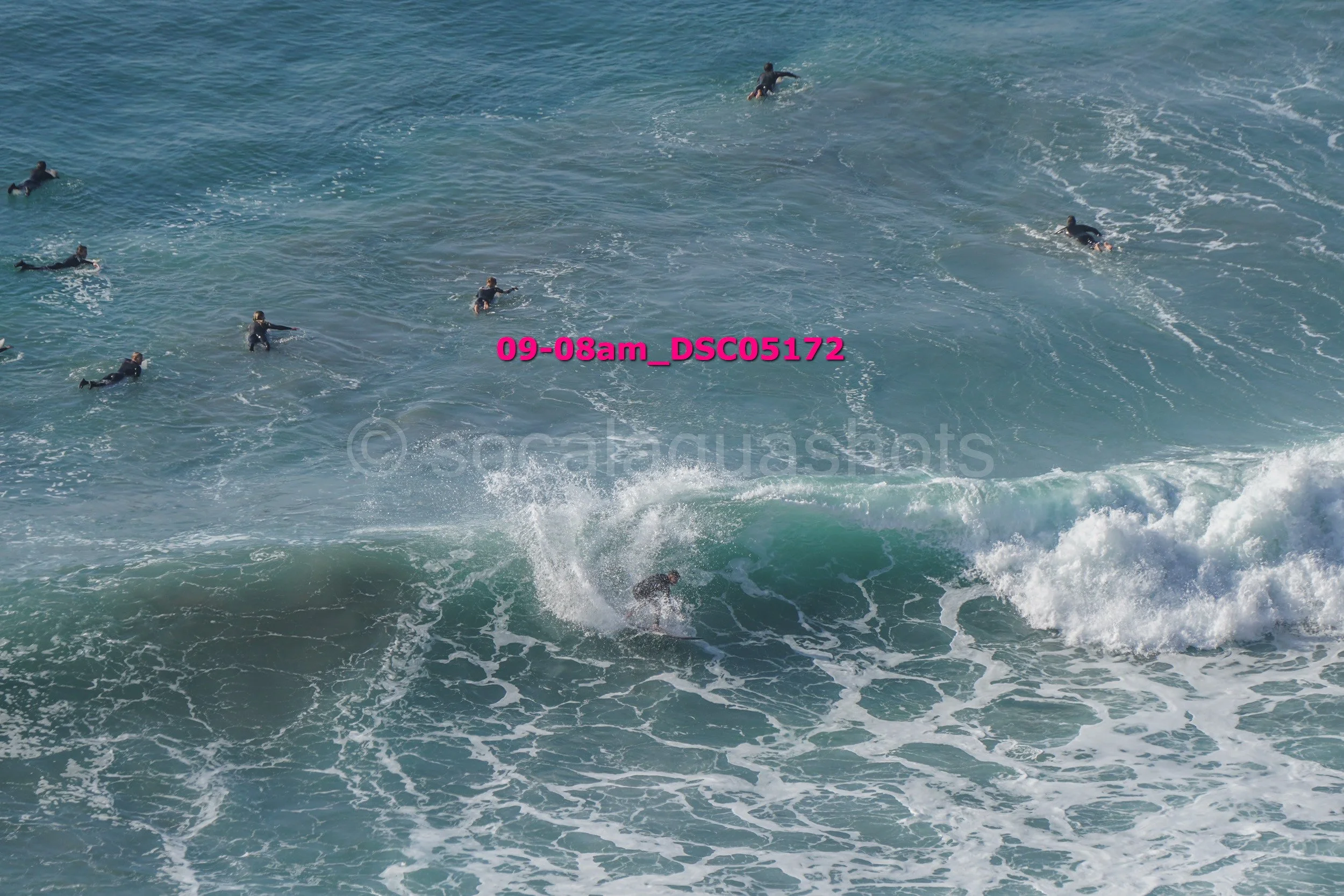 A group of surfers in wetsuits riding and waiting on waves in the ocean.