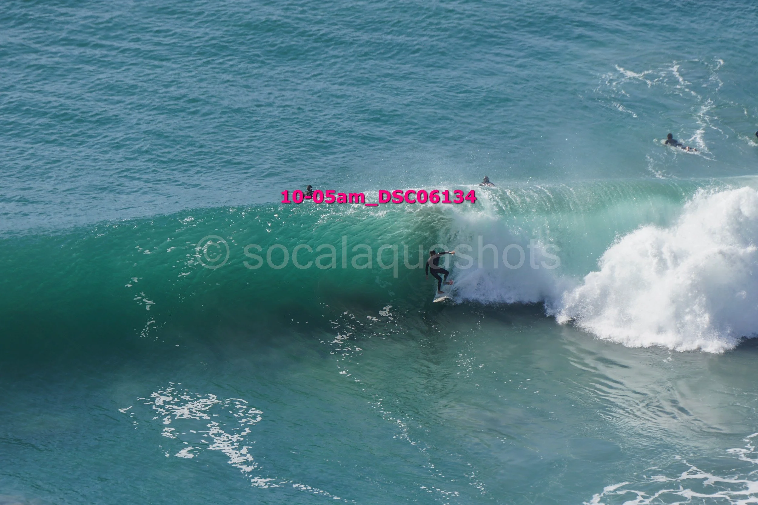 Surfer riding a large wave in the ocean with other surfers in the distance.