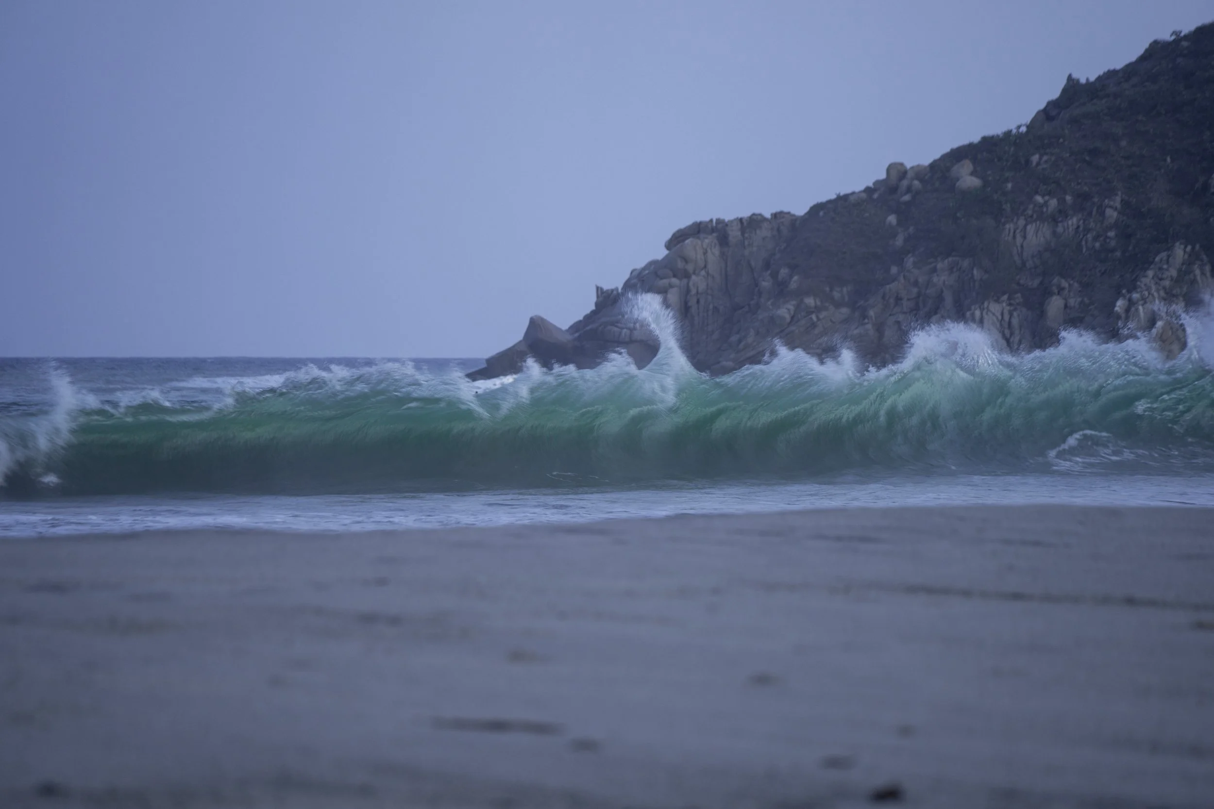 Waves crashing against a rocky shoreline under a cloudy sky.