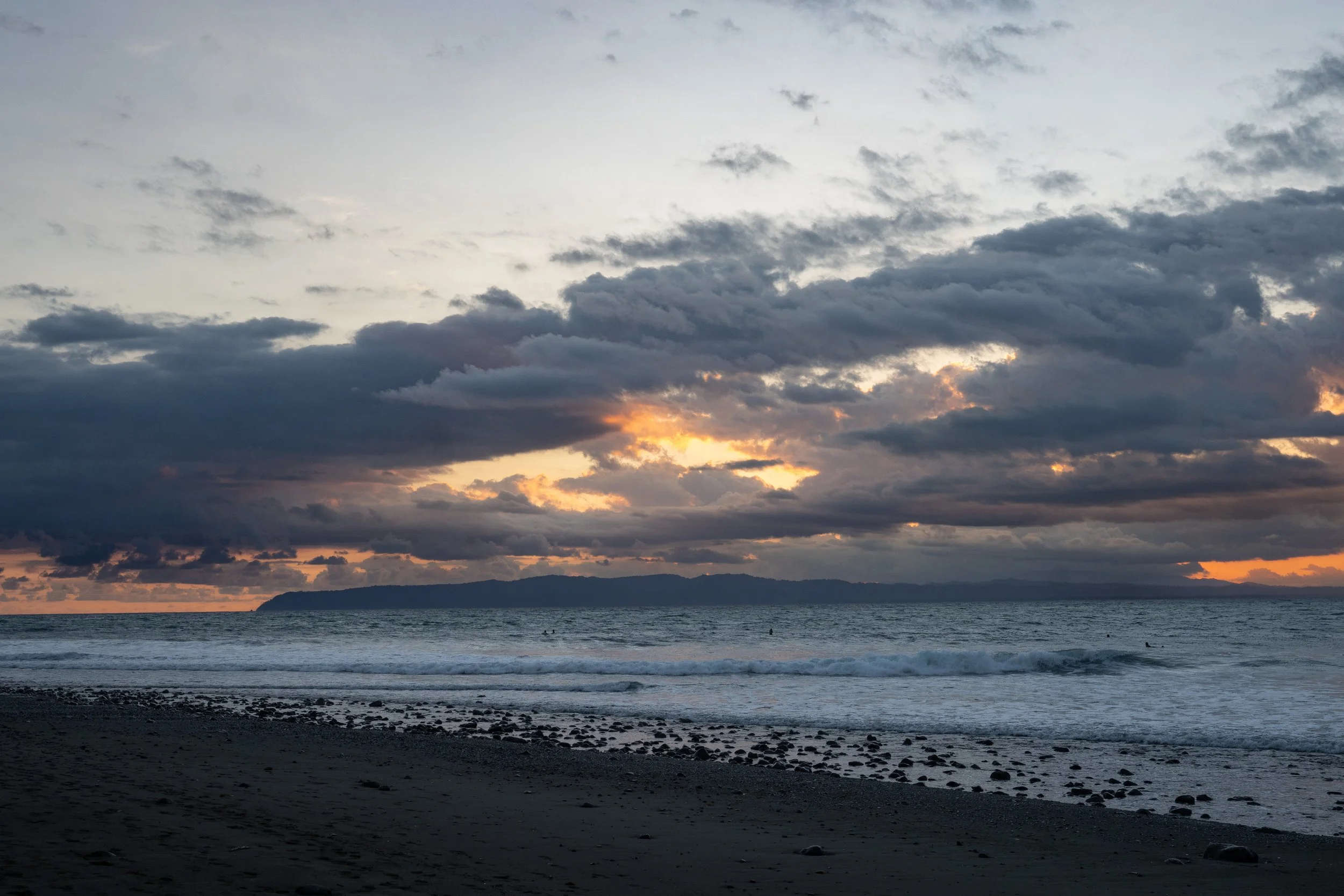A sunset over the ocean with a cloudy sky and land in the distance.
