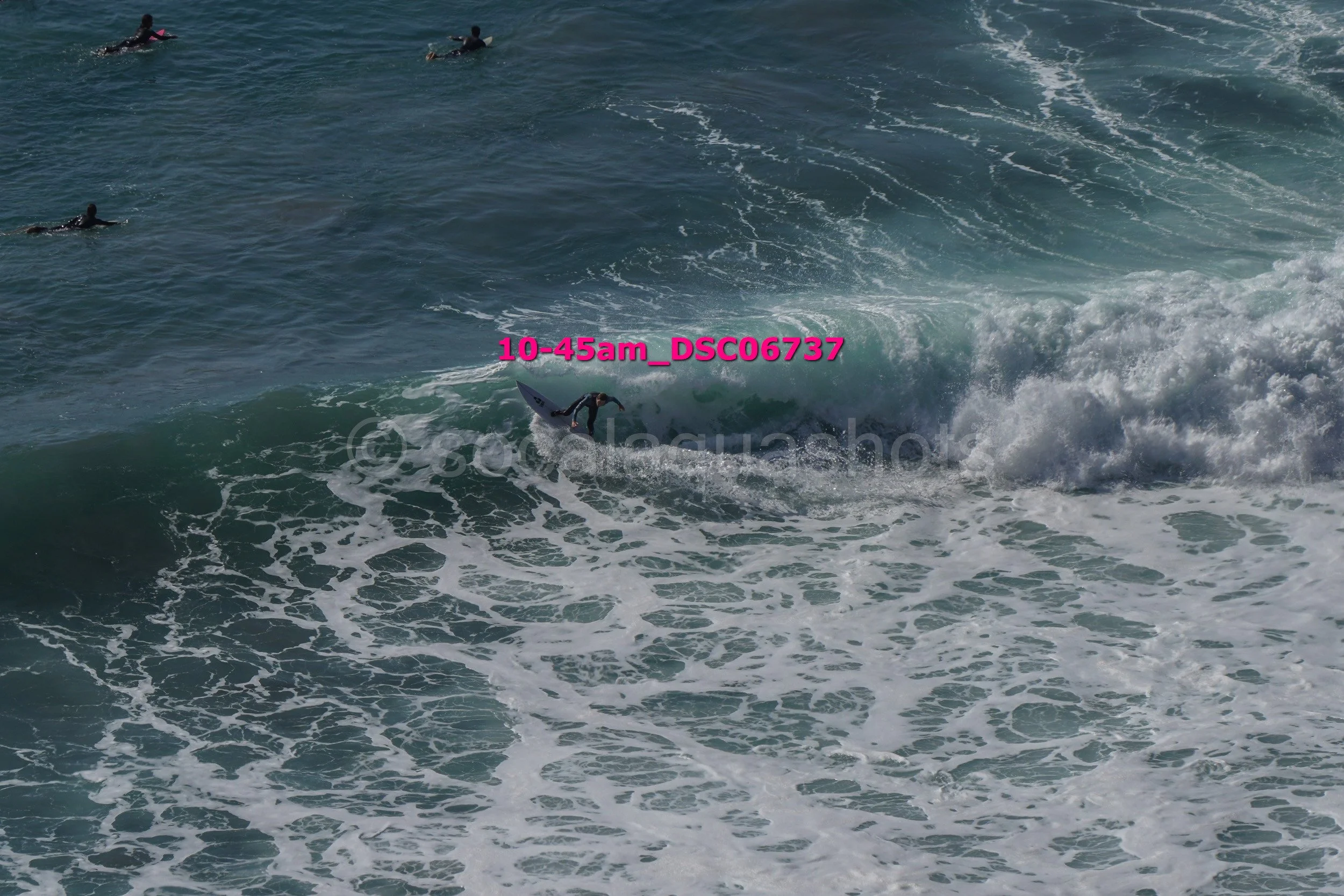 A person surfing on a wave in the ocean with several other surfers in the background.