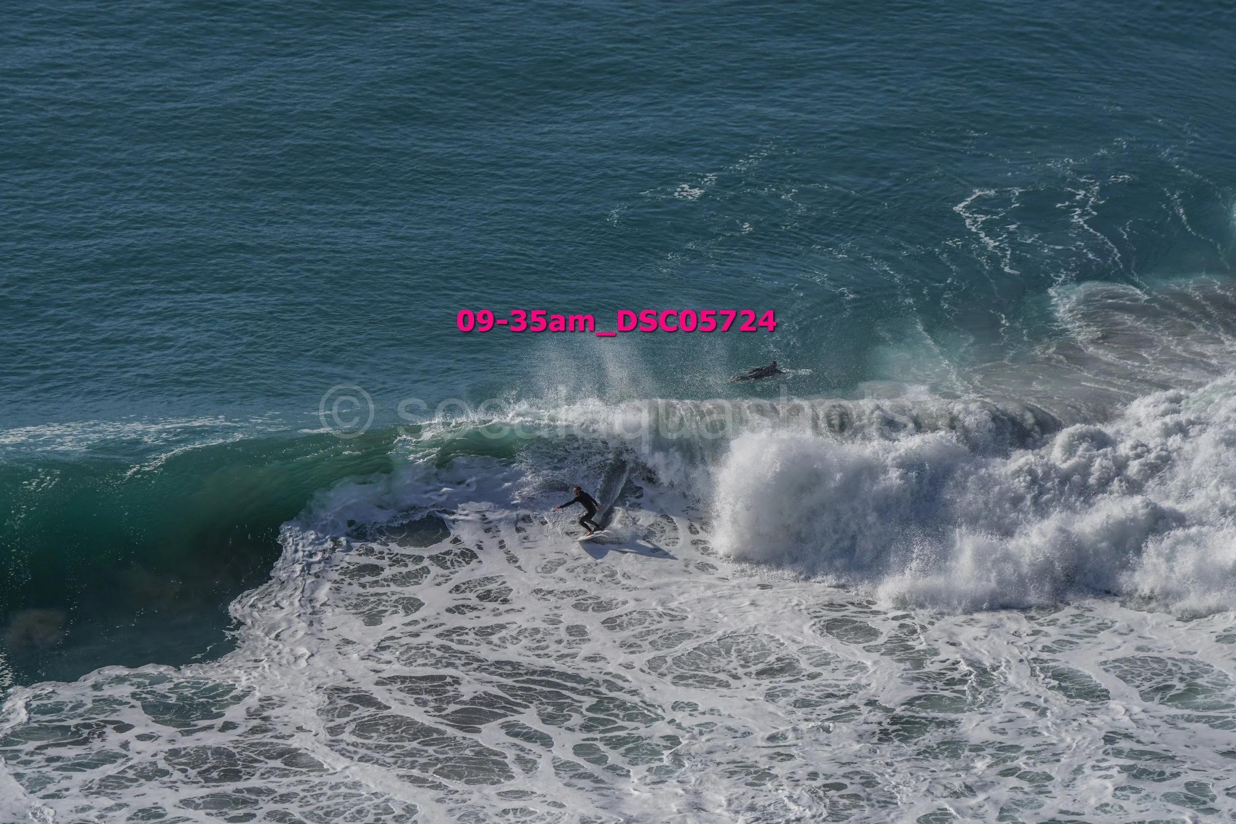 Surfer riding a wave in the ocean with another surfer visible in the background.