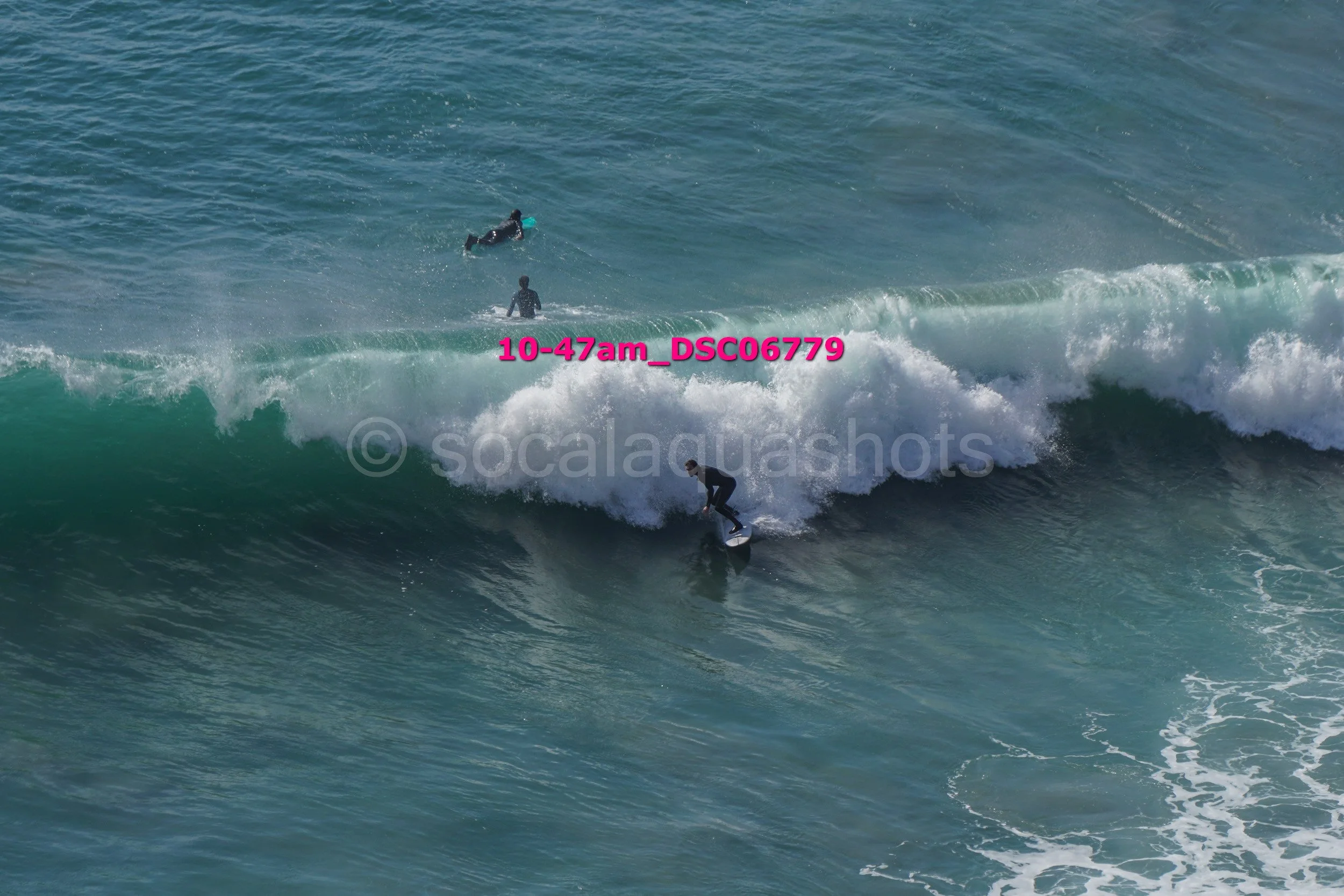 Surfer riding a wave with two people swimming in the background.