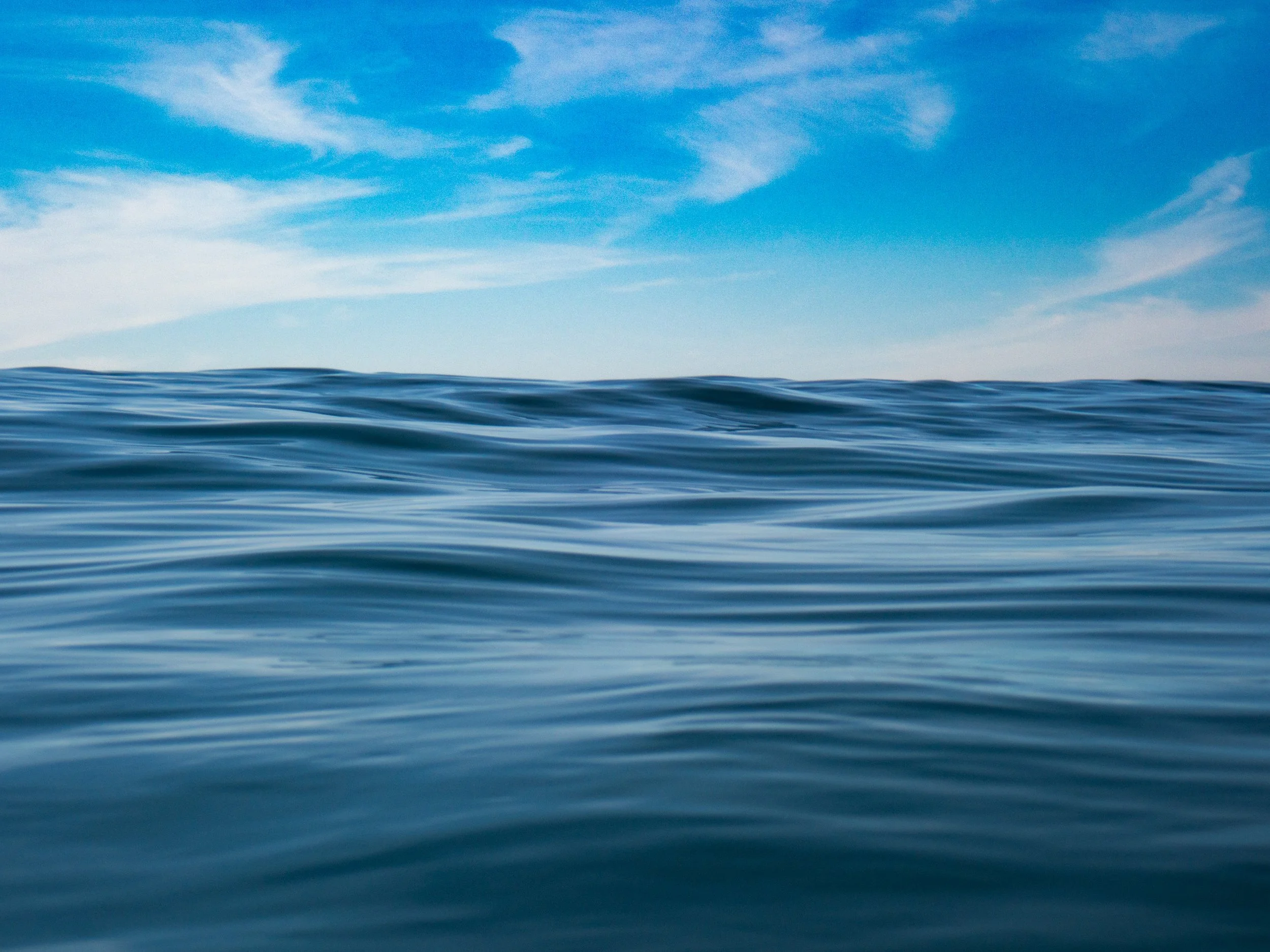 Ocean waves under a blue sky with scattered clouds.