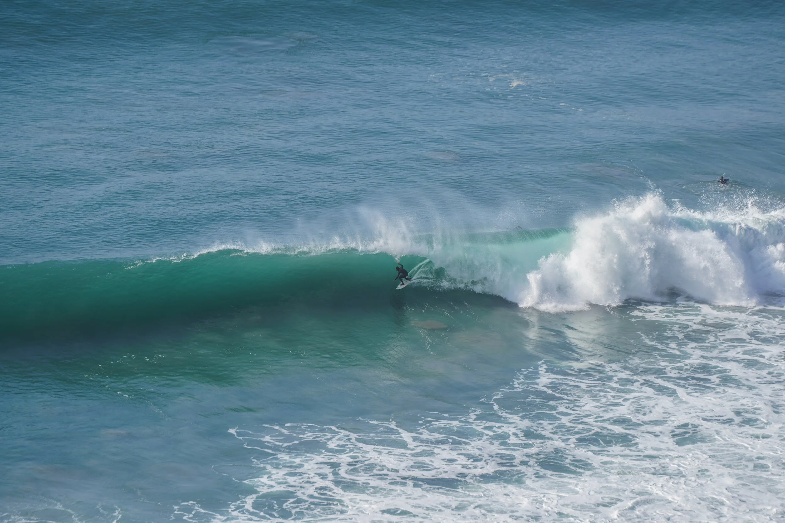 Surfer riding a wave in the ocean with blue water and white foam.