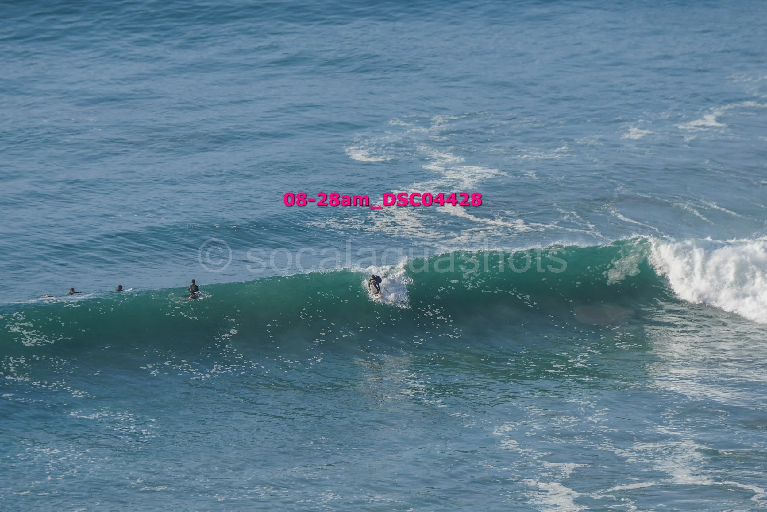 A person surfing on a large wave in the ocean with three other surfers in the water nearby.
