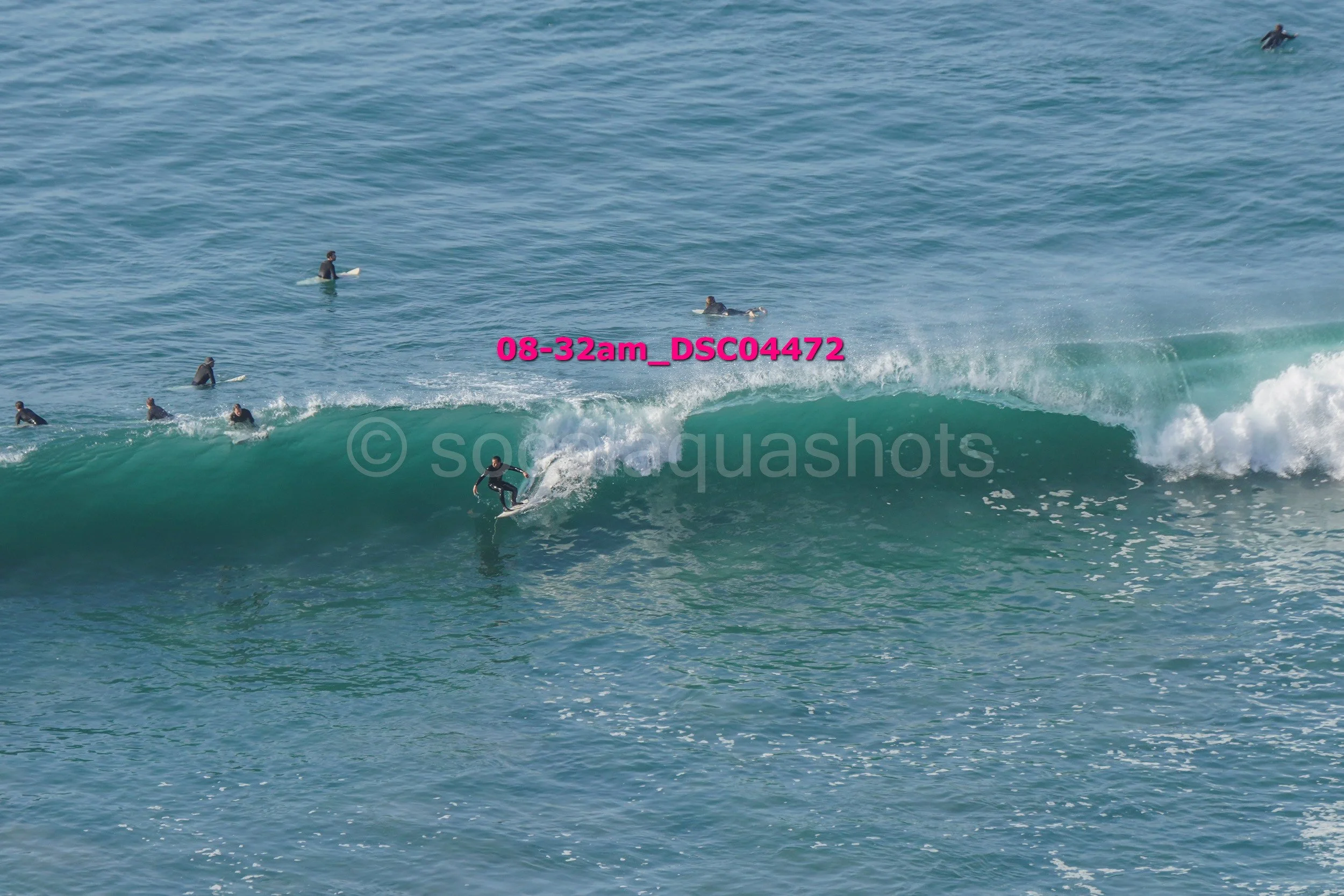 Surfer riding a large wave in the ocean with several surfers in the background.