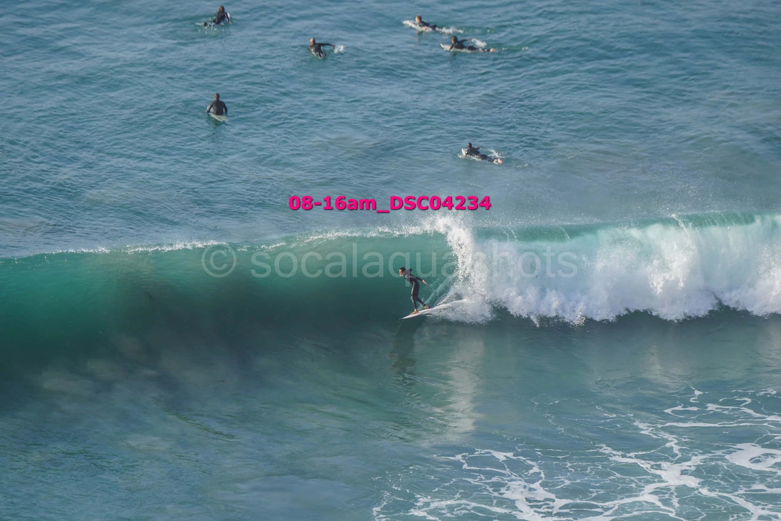 A person surfing on a wave in the ocean, with several other surfers in the water in the background.