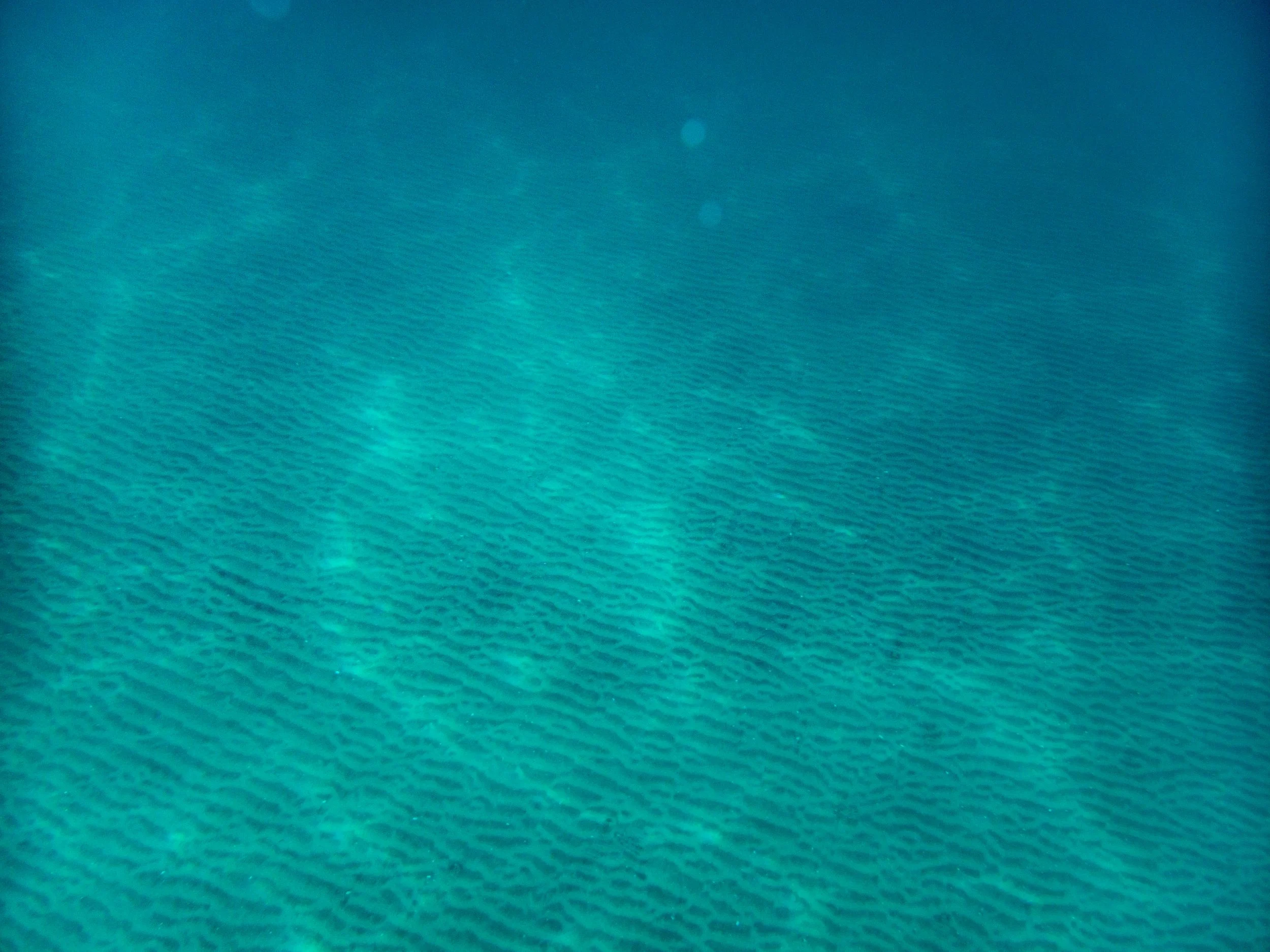Aerial view of clear turquoise ocean water with visible patterns on the seabed.
