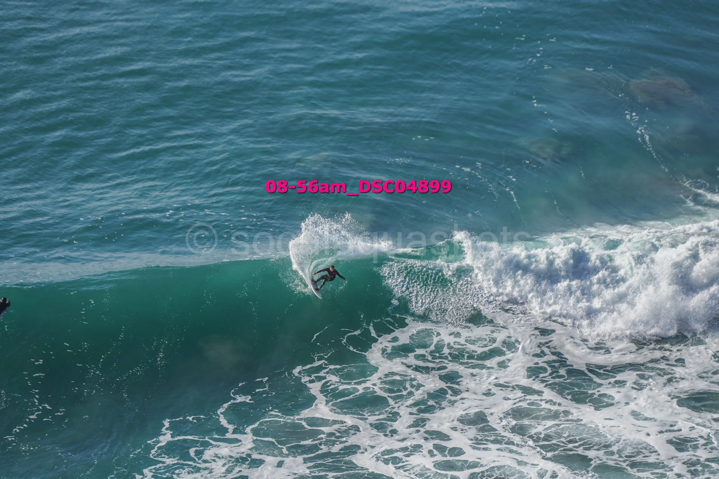 A person surfing on a wave in the ocean with white foam and water spray, wearing a wetsuit.
