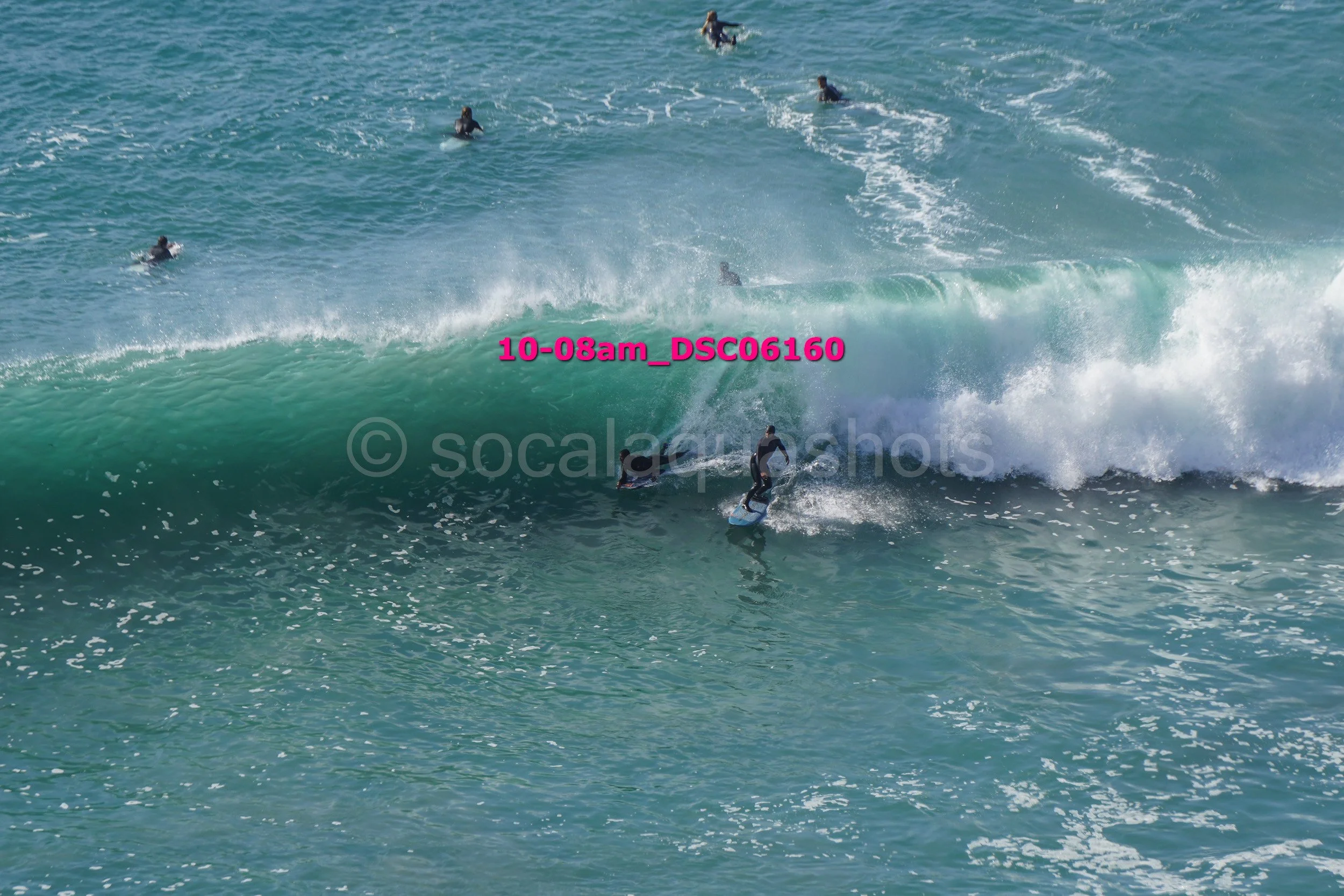 Surfers riding a large wave with several other surfers in the water, ocean scene.