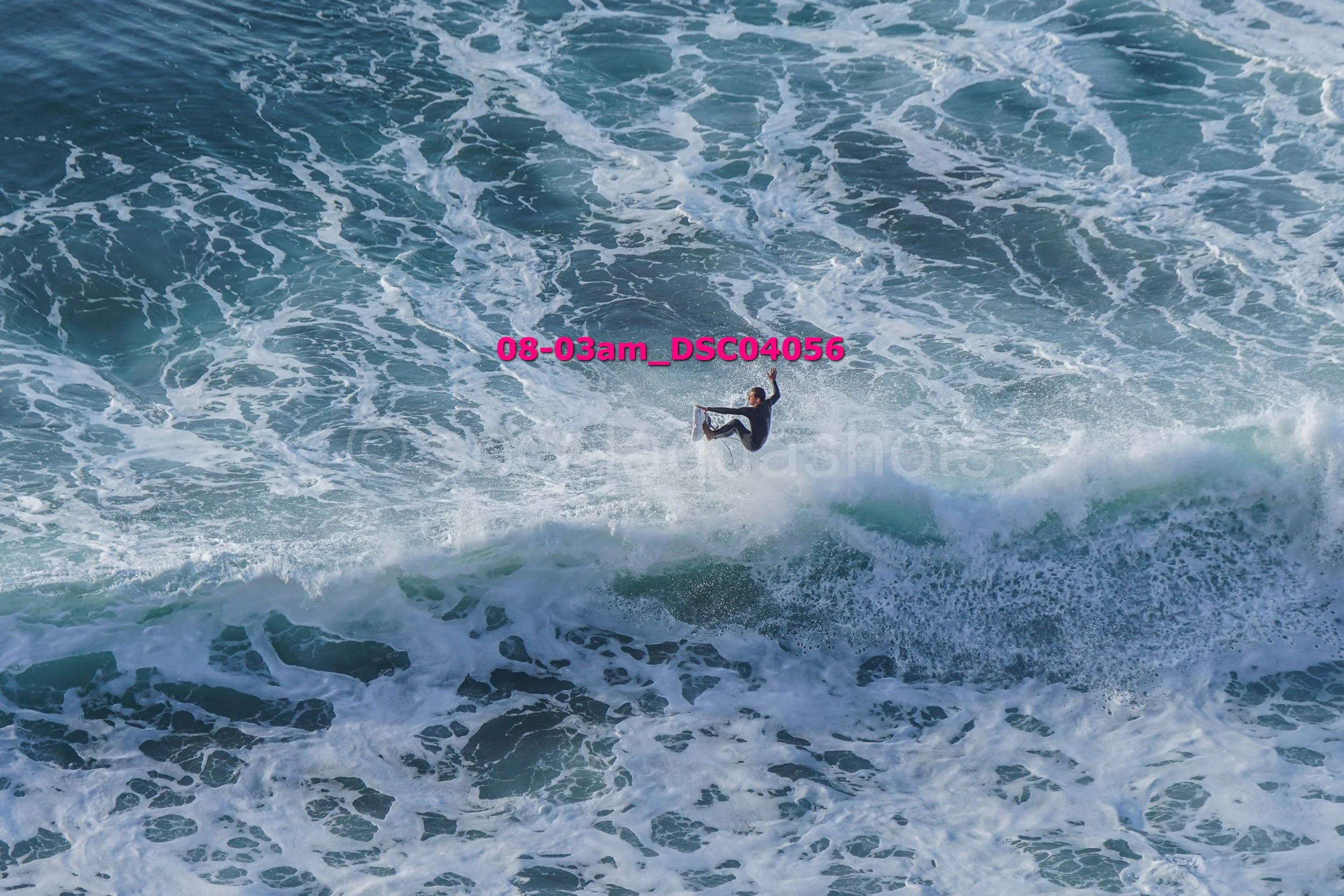 Person performing a trick on a surfboard amid crashing ocean waves.
