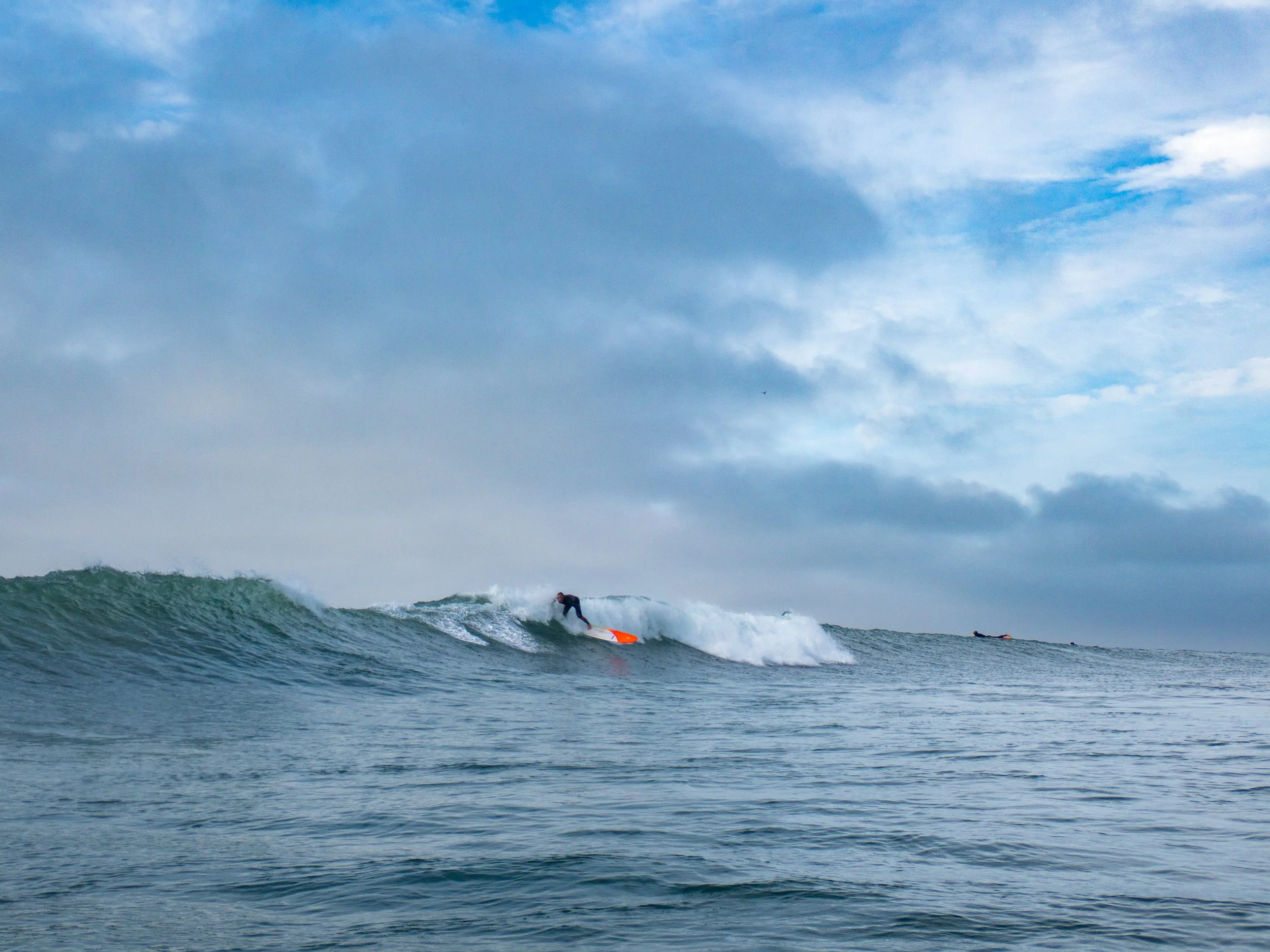 A person surfing on a wave in the ocean under a partly cloudy sky.