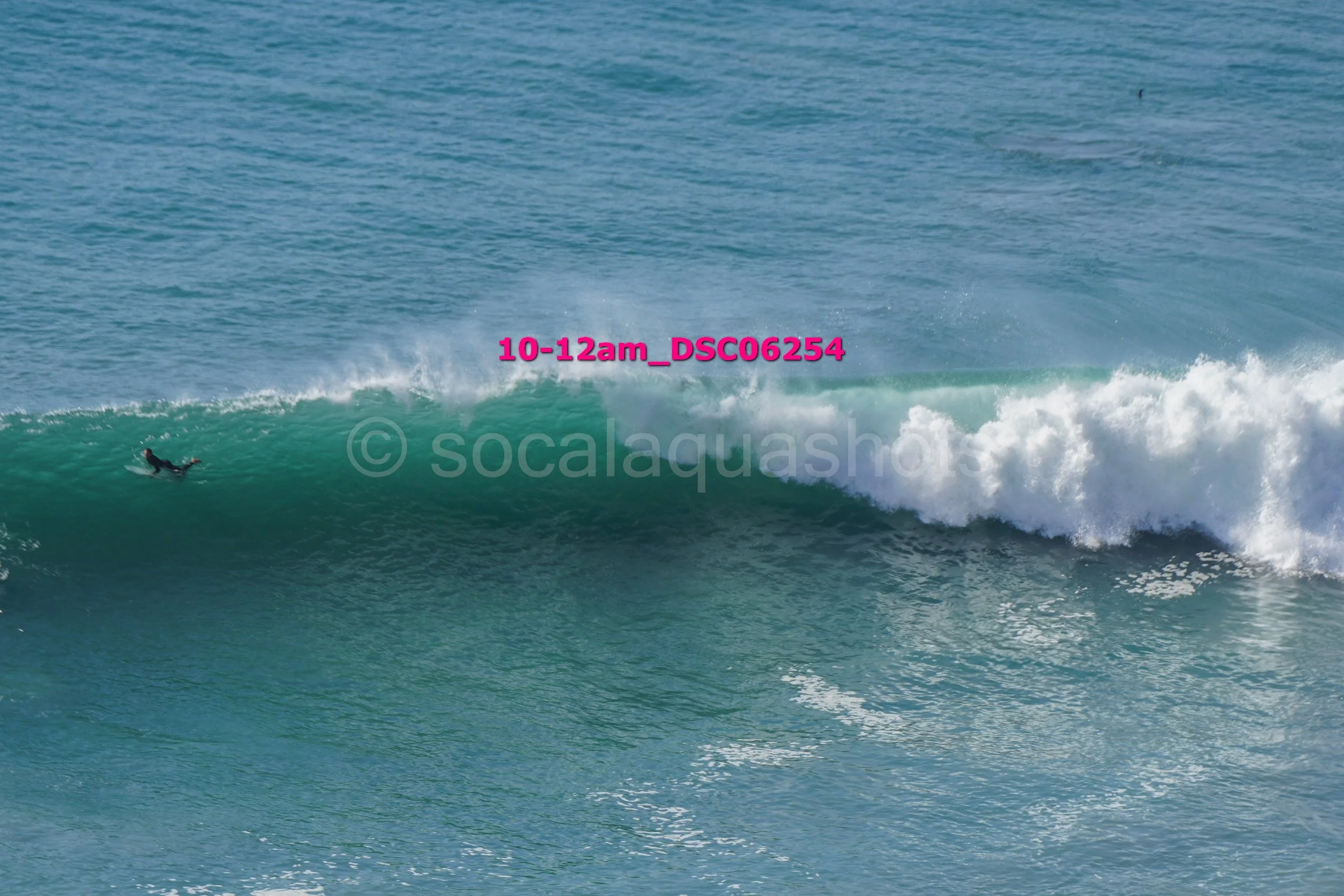 A person surfing a large wave in the ocean during daylight with visible spray.