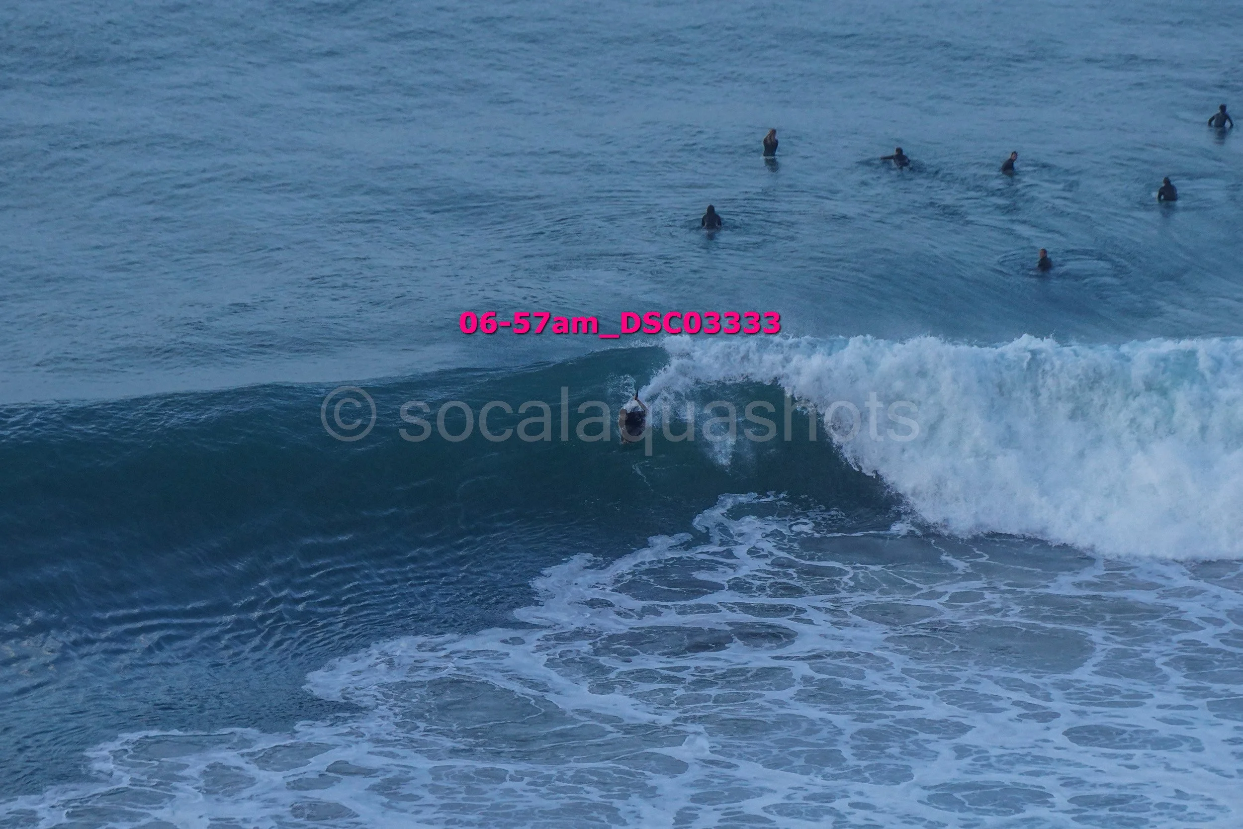 Surfer riding a wave in the ocean with several people swimming in the background.