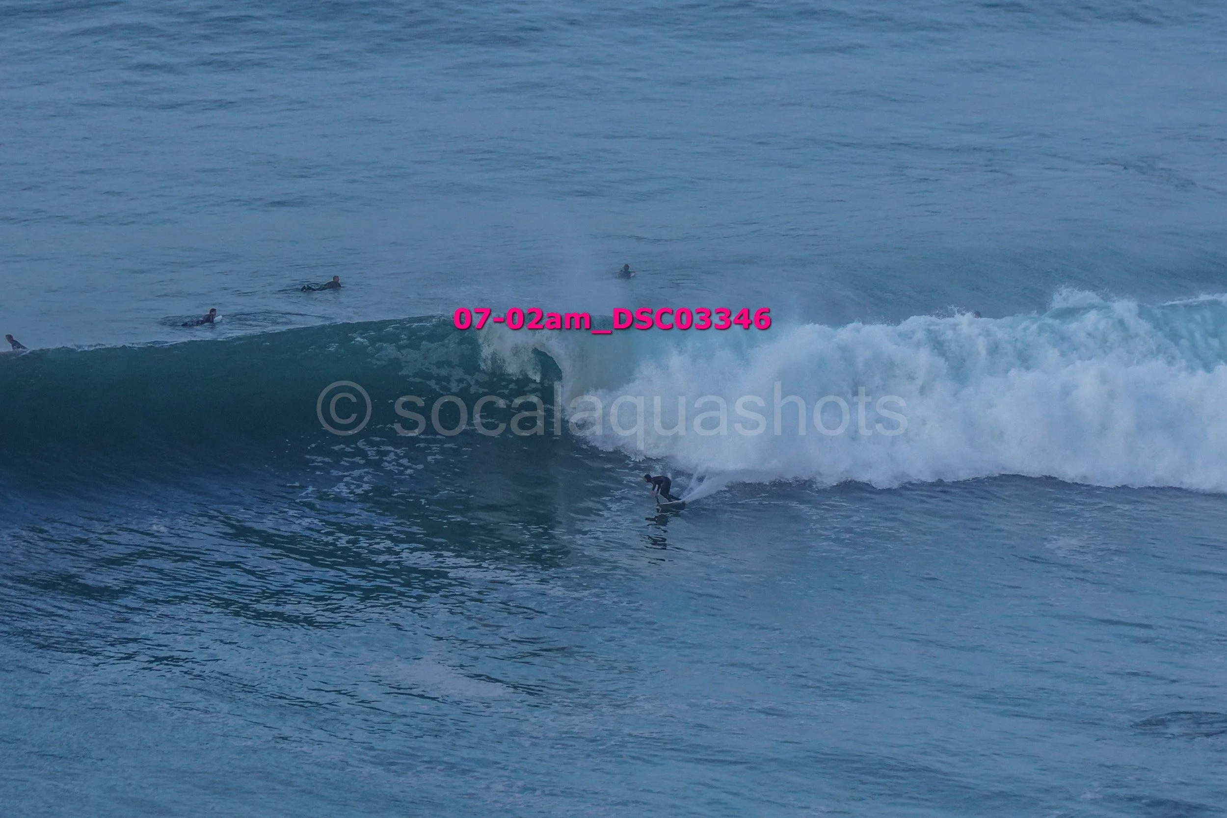 A person surfing on a wave with three other surfers in the background in the ocean.