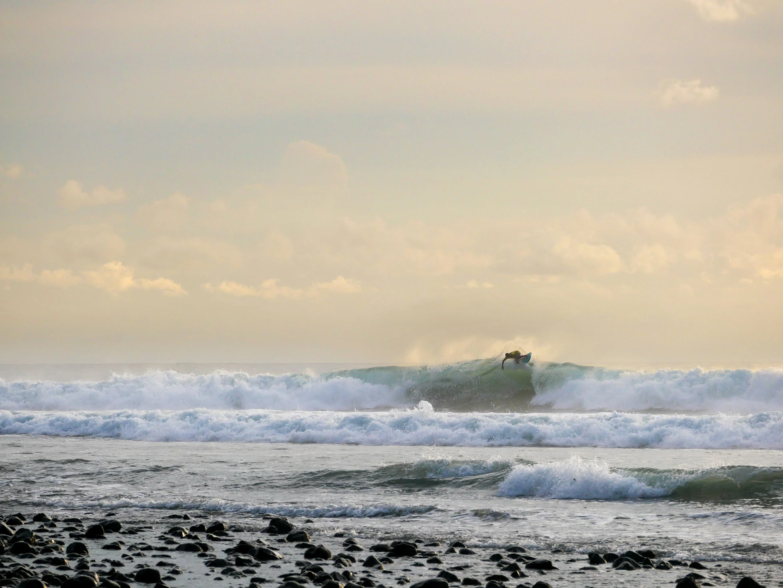 Person surfing on ocean wave with cloudy sky and rocky shoreline