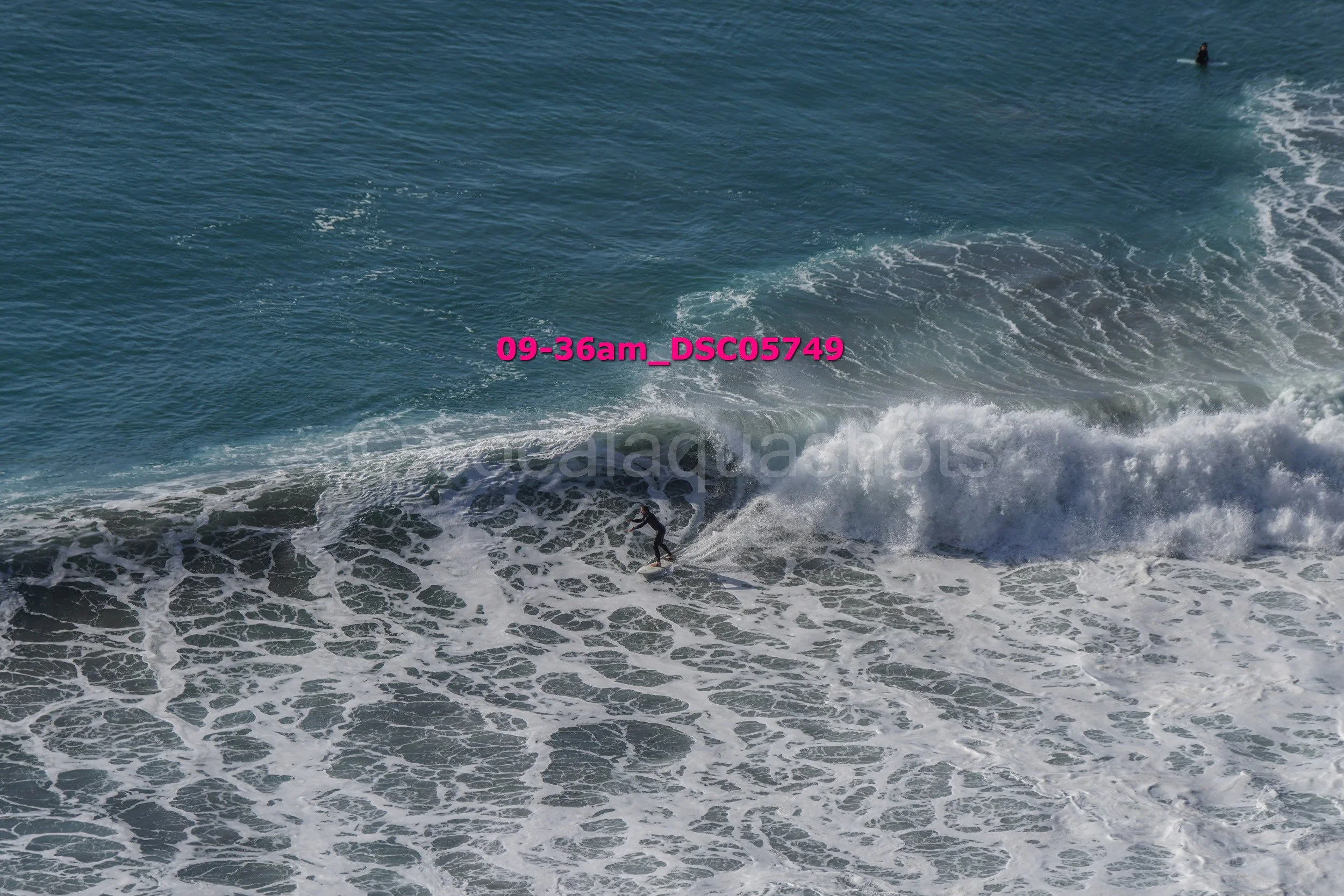 Surfer riding a wave in the ocean, with another person in the water in the background.