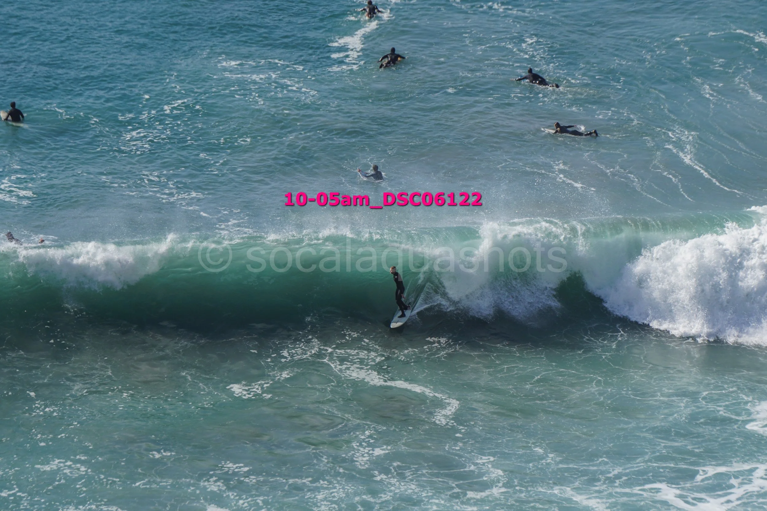 A person surfing on a wave with several other people swimming and surfing in the ocean in the background.