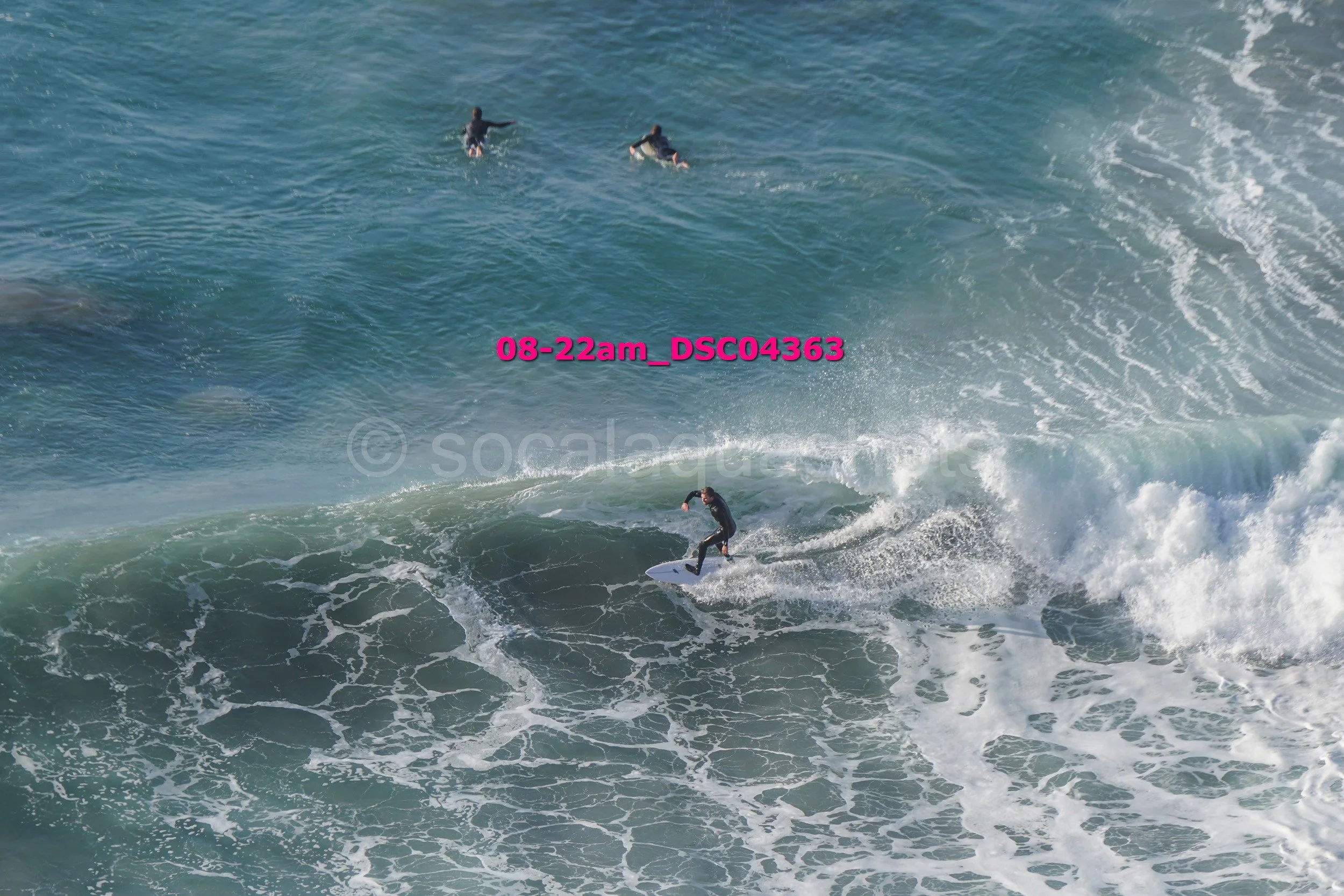 Surfer riding a wave with three other surfers in the distance in the ocean.